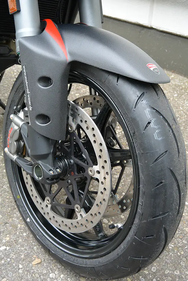 Vorderreifen und Bremsanlage eines Motorrads mit Carbon-Kotflügel.