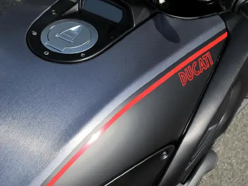 Eine Nahaufnahme eines Ducati-Motorradtanks mit rotem Logo und Streifen.