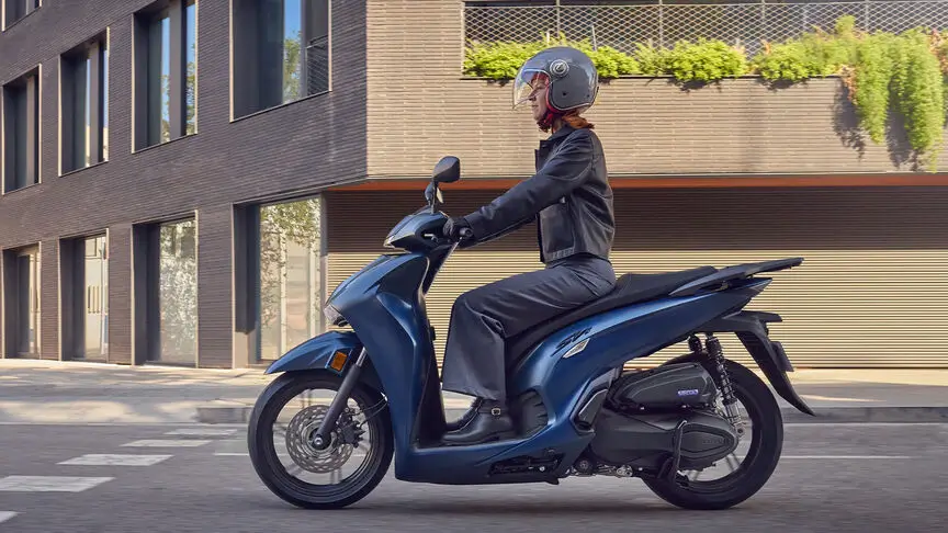 Eine Person fährt einen blauen Honda SH350i Roller auf einer Stadtstraße.