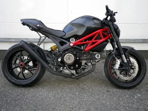 Ein schwarzes Motorrad mit rotem Rahmen, vermutlich eine Ducati, steht seitlich auf einer Straße.