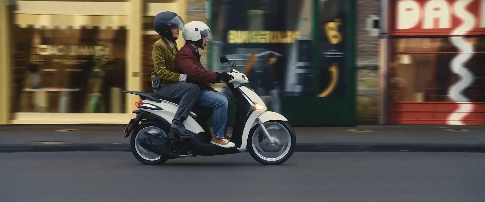 LIBERTY Zwei Personen fahren auf einem weißen Liberty-Roller durch die Stadt.