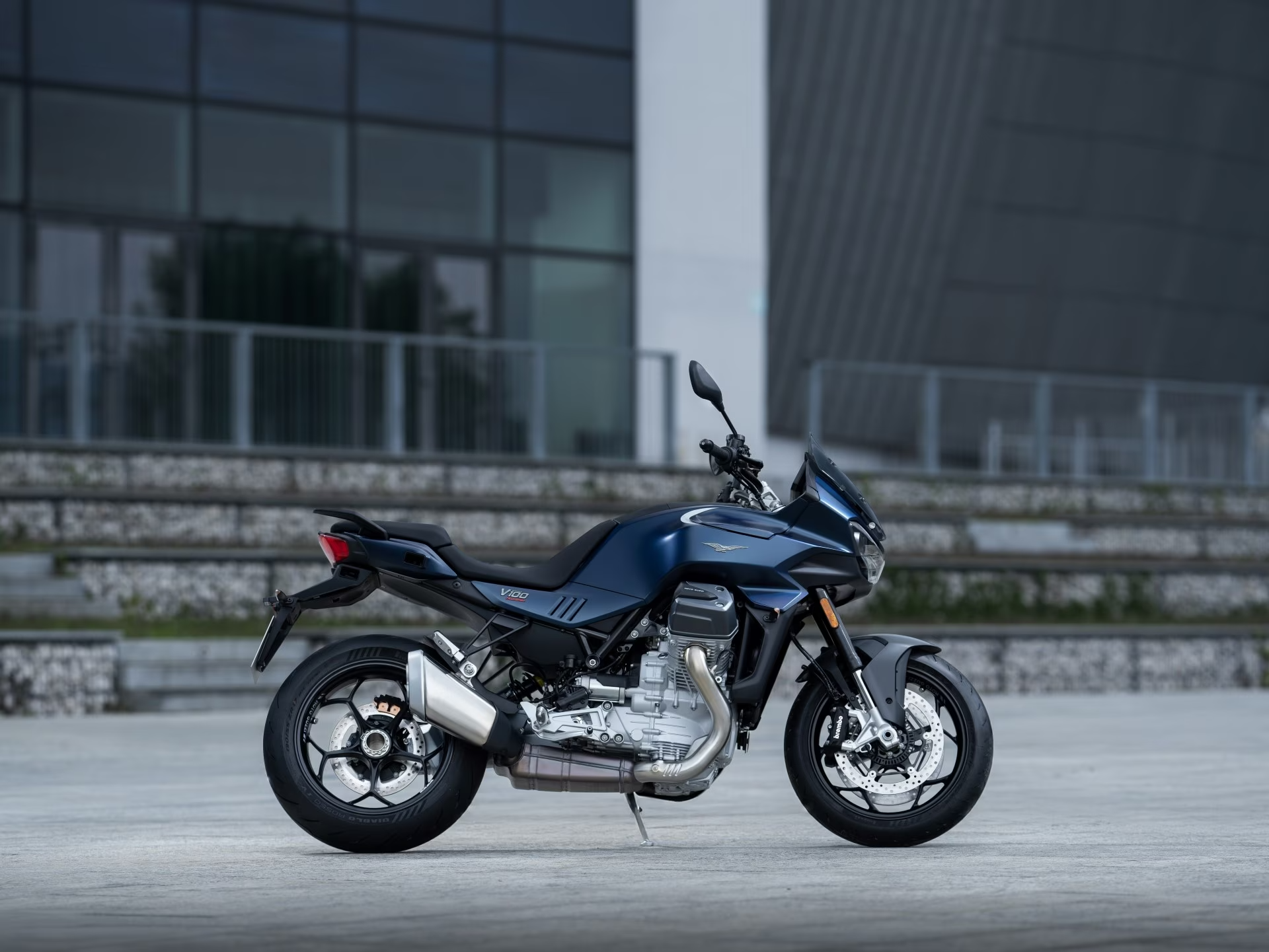 Ein blaues Moto Guzzi V100 Mandello Motorrad steht vor einem modernen Gebäude.
