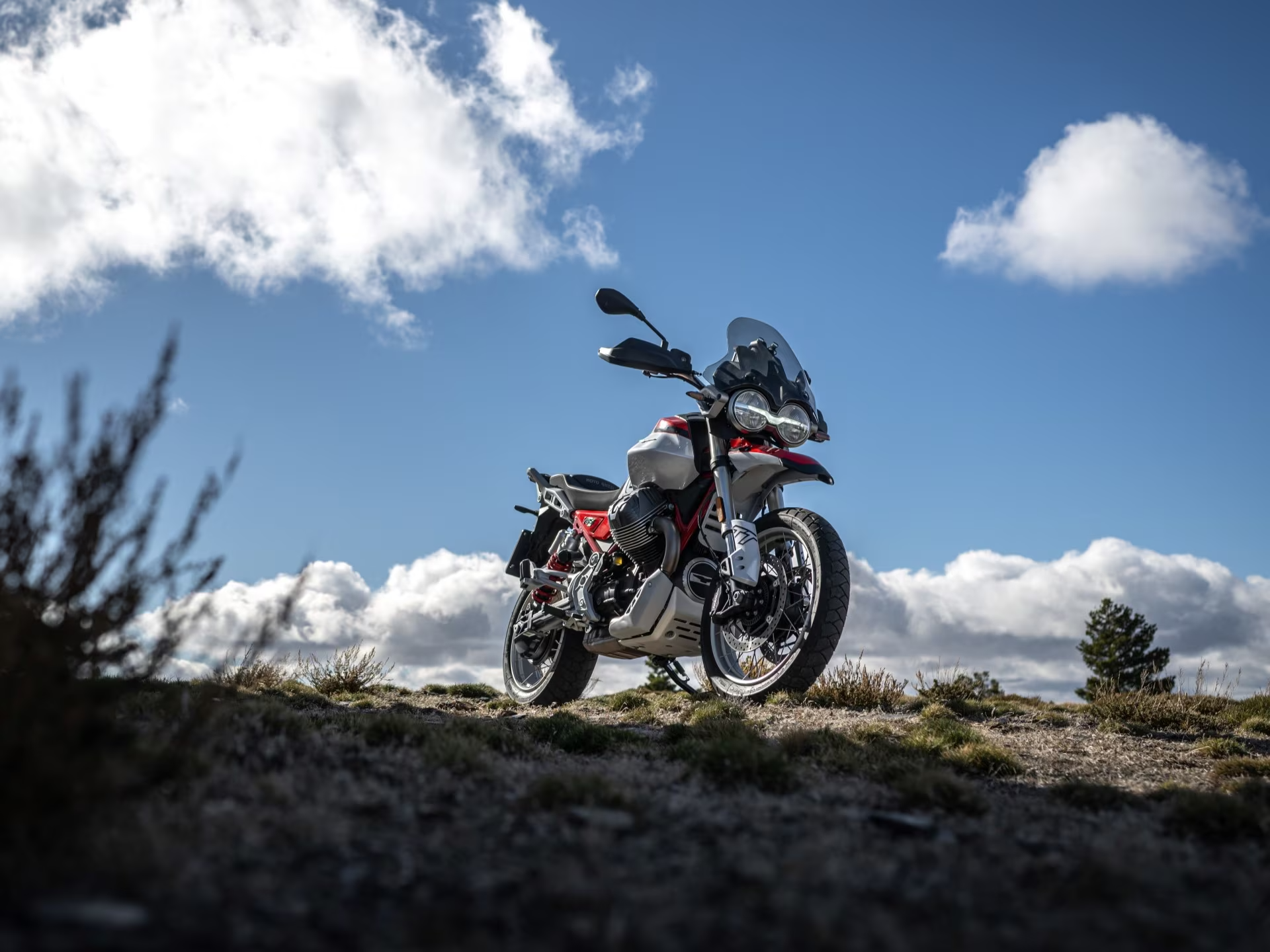 Motorrad Moto Guzzi V85 TT steht auf einer offenen Landschaft unter einem blauen Himmel mit Wolken.
