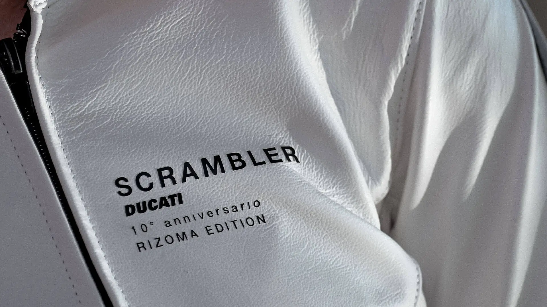 Nahaufnahme eines weißen Lederjackets mit der Aufschrift "Scrambler Ducati 10° Anniversario Rizoma Edition".