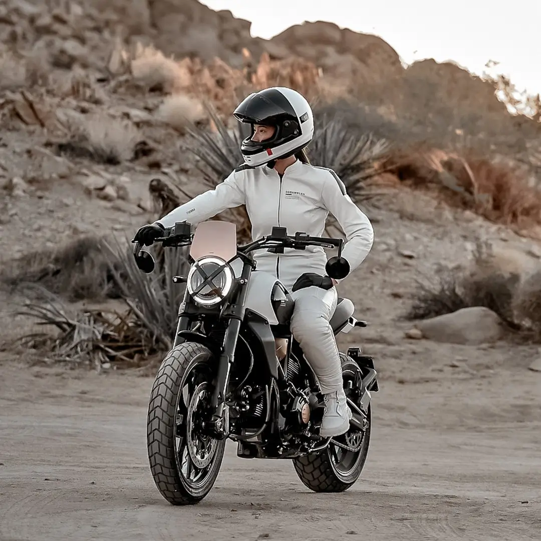 Eine Person auf einer Ducati Scrambler 10° Anniversario Rizoma Edition fährt durch eine Wüstenlandschaft.