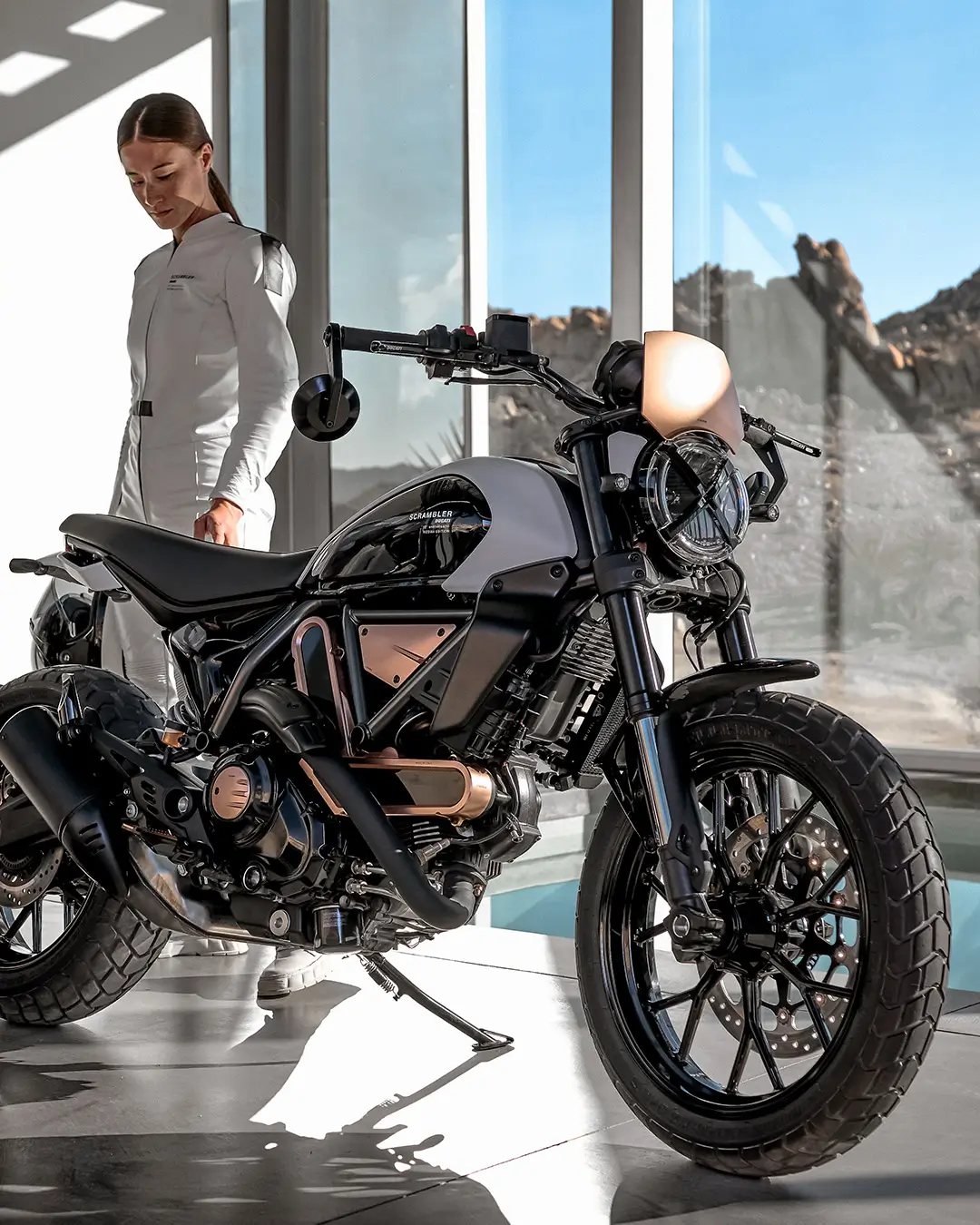 Eine Person steht neben einem Scrambler Ducati Motorrad in einem modernen Raum.