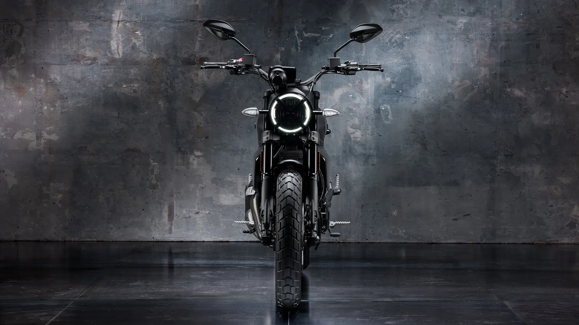 Frontansicht eines Scrambler Icon Dark Motorrads vor einer grauen Wand.
