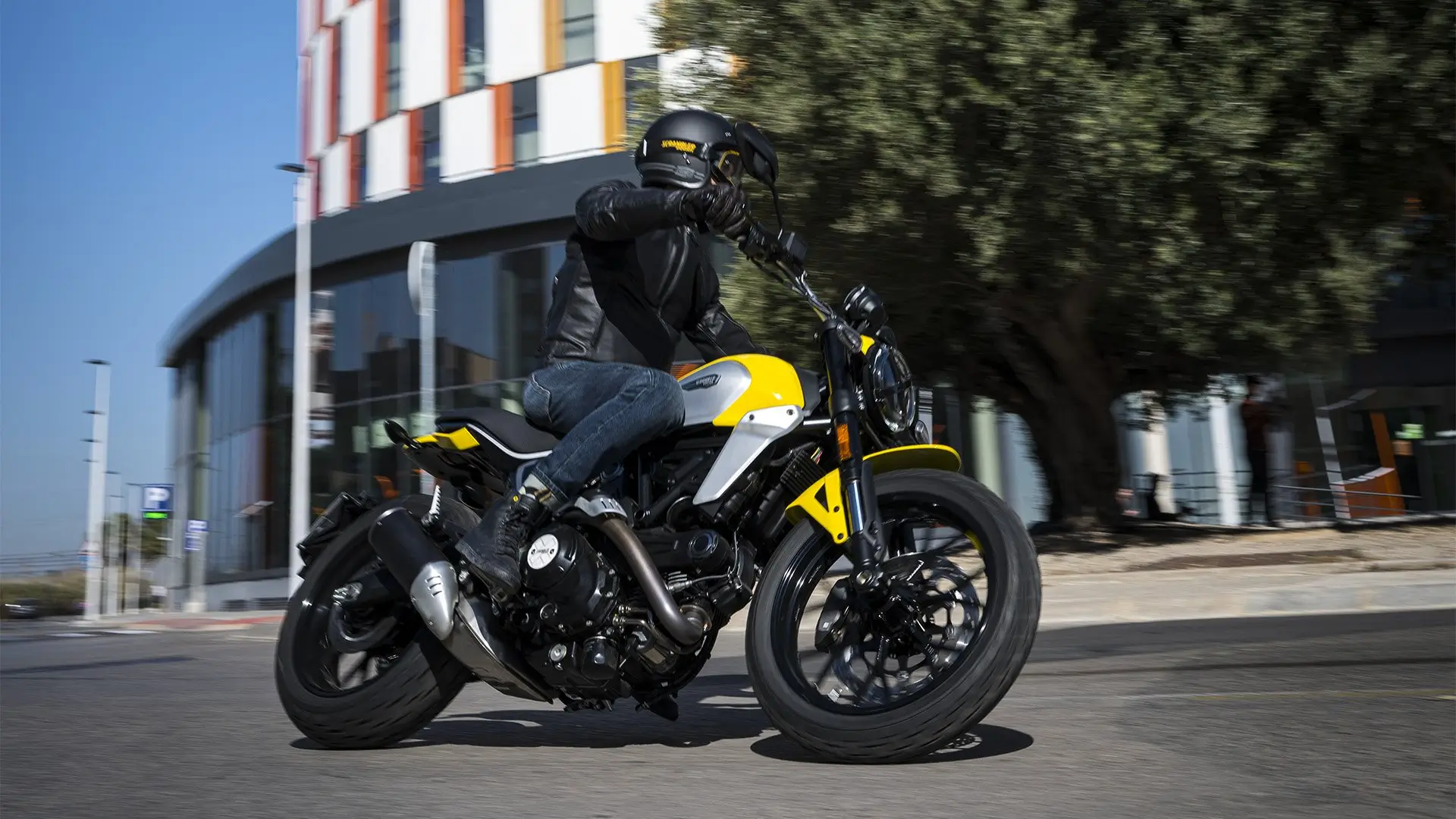 Ein Motorradfahrer fährt eine gelb-schwarze Scrambler Icon Next Gen auf einer Straße.