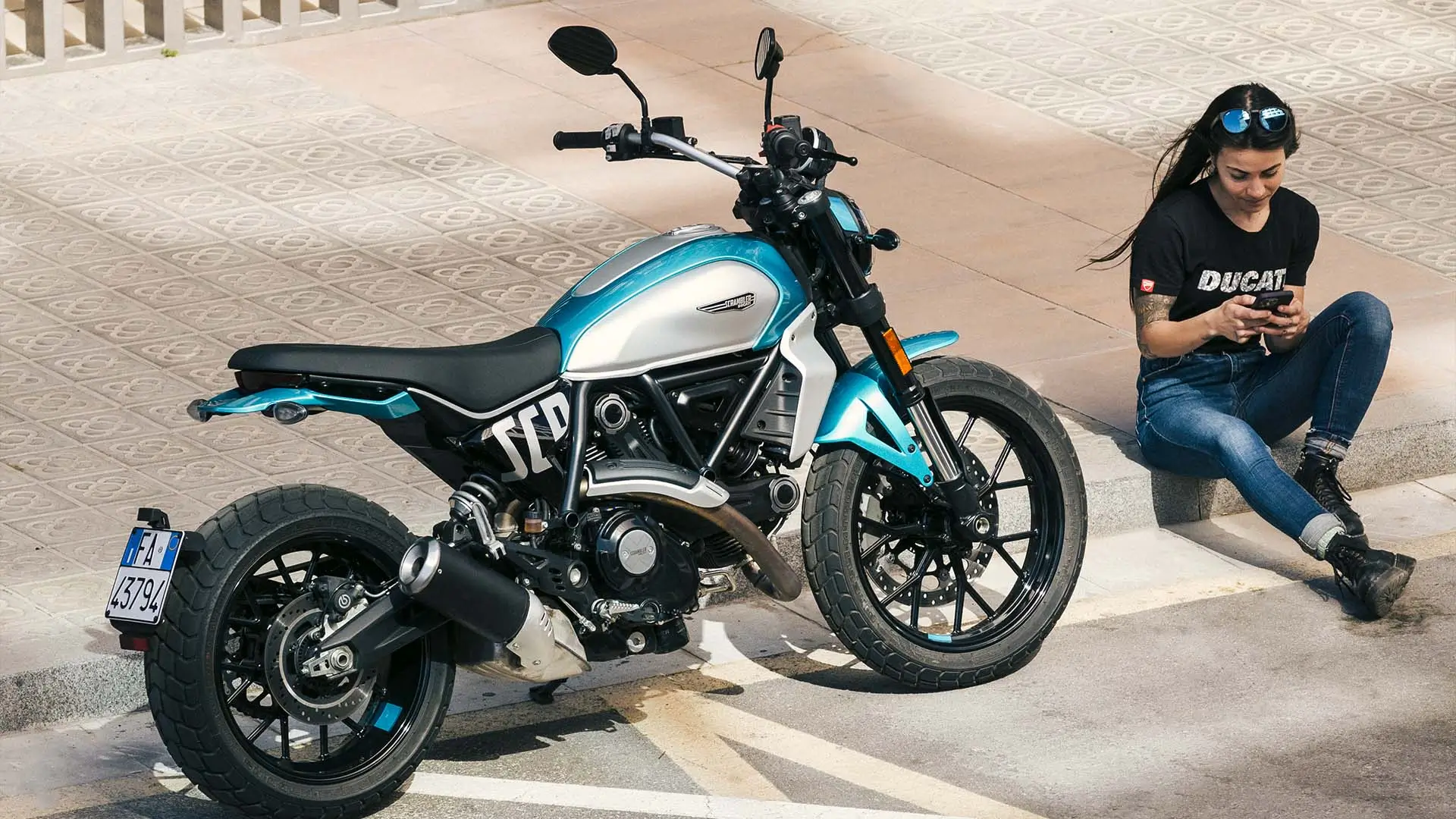 Ducati Scrambler Icon Next-Gen Motorrad neben einer sitzenden Person, die ein Smartphone benutzt.