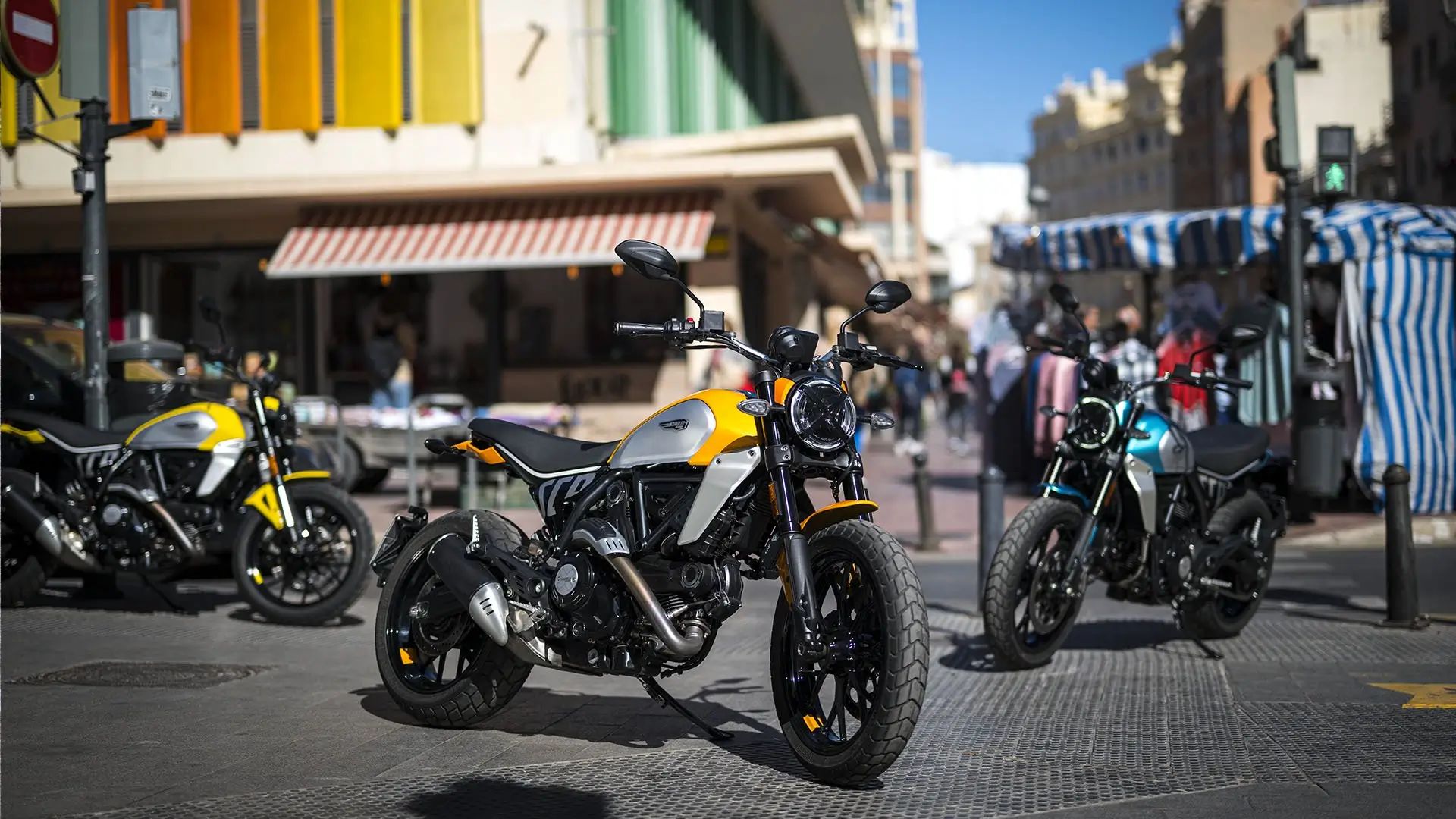 Drei Ducati Scrambler Icon Motorräder stehen auf einem belebten städtischen Platz.