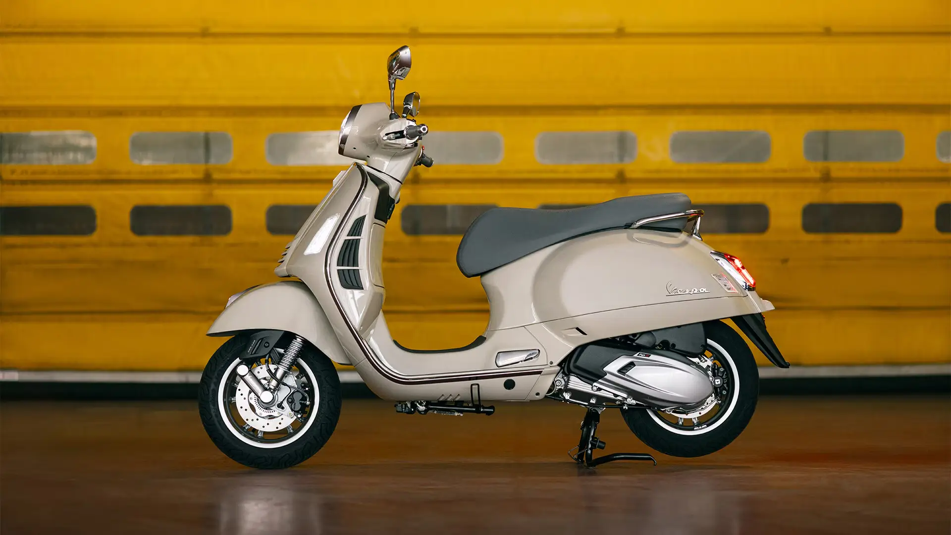 Vespa GTS Roller in Beige vor einer gelben Wand.