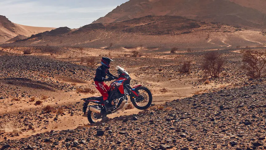 Ein Motorradfahrer fährt eine Honda Africa Twin durch eine steinige Wüstenlandschaft.