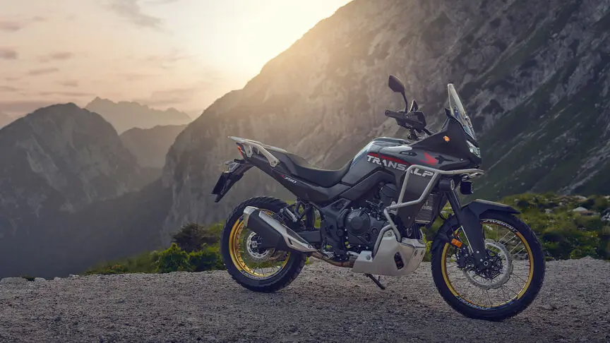 Ein Honda Transalp Motorrad steht vor einer Berglandschaft bei Sonnenuntergang.