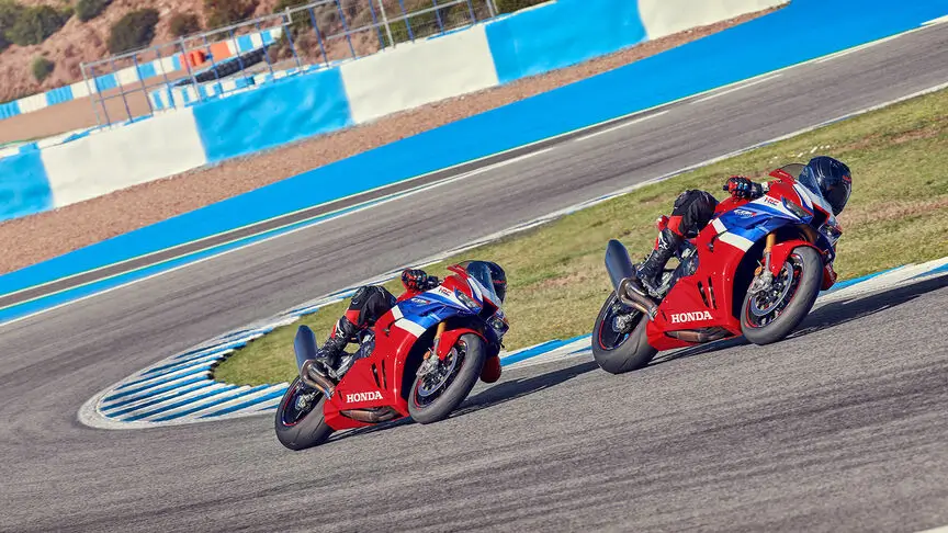 c4 (2) Zwei rote Honda-Motorräder fahren in Schräglage auf einer Rennstrecke.