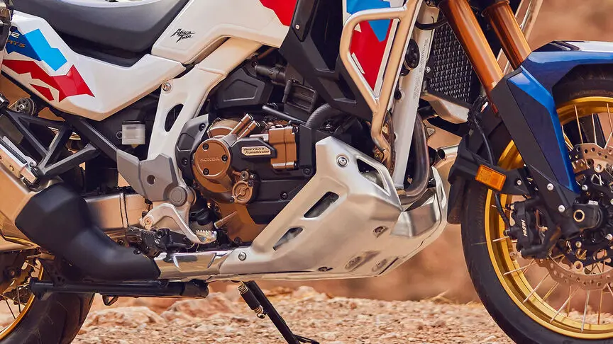 c4 (3) Ein Motorrad mit sichtbarem Motor und Vorderrad auf einem sandigen Untergrund.