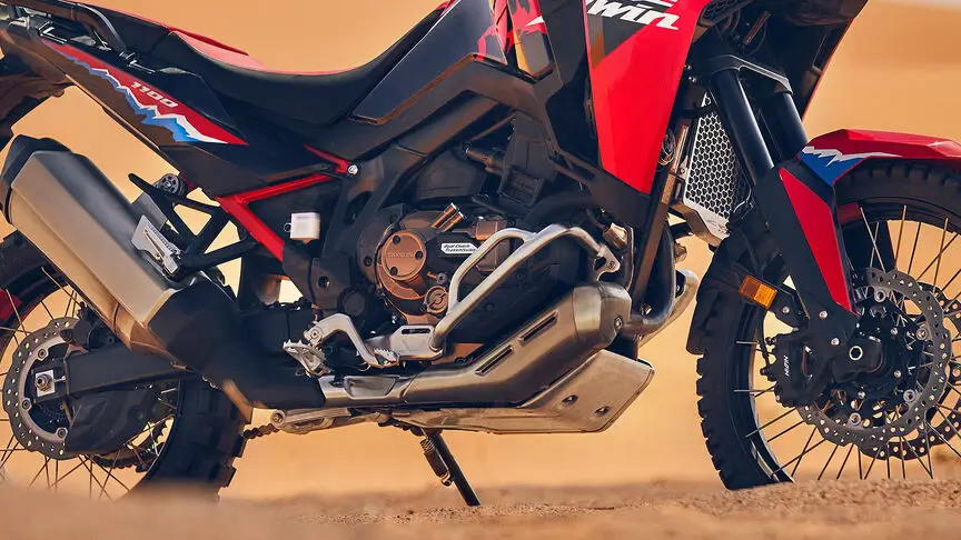 c4 (3) Ein rotes Motorrad Honda Africa Twin steht auf sandigem Untergrund.