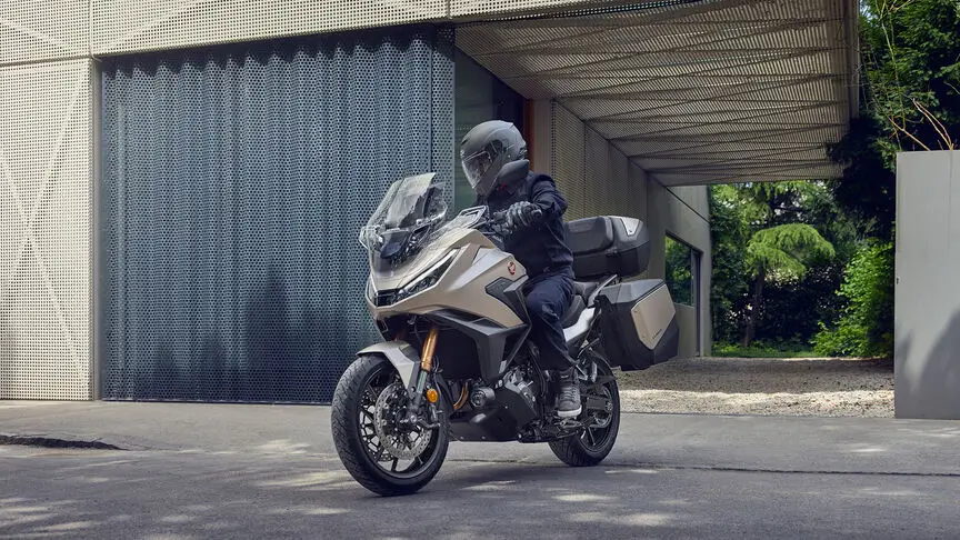 c4 (3) Ein Motorradfahrer auf einer Honda NT1100 fährt vor einem modernen Gebäude.