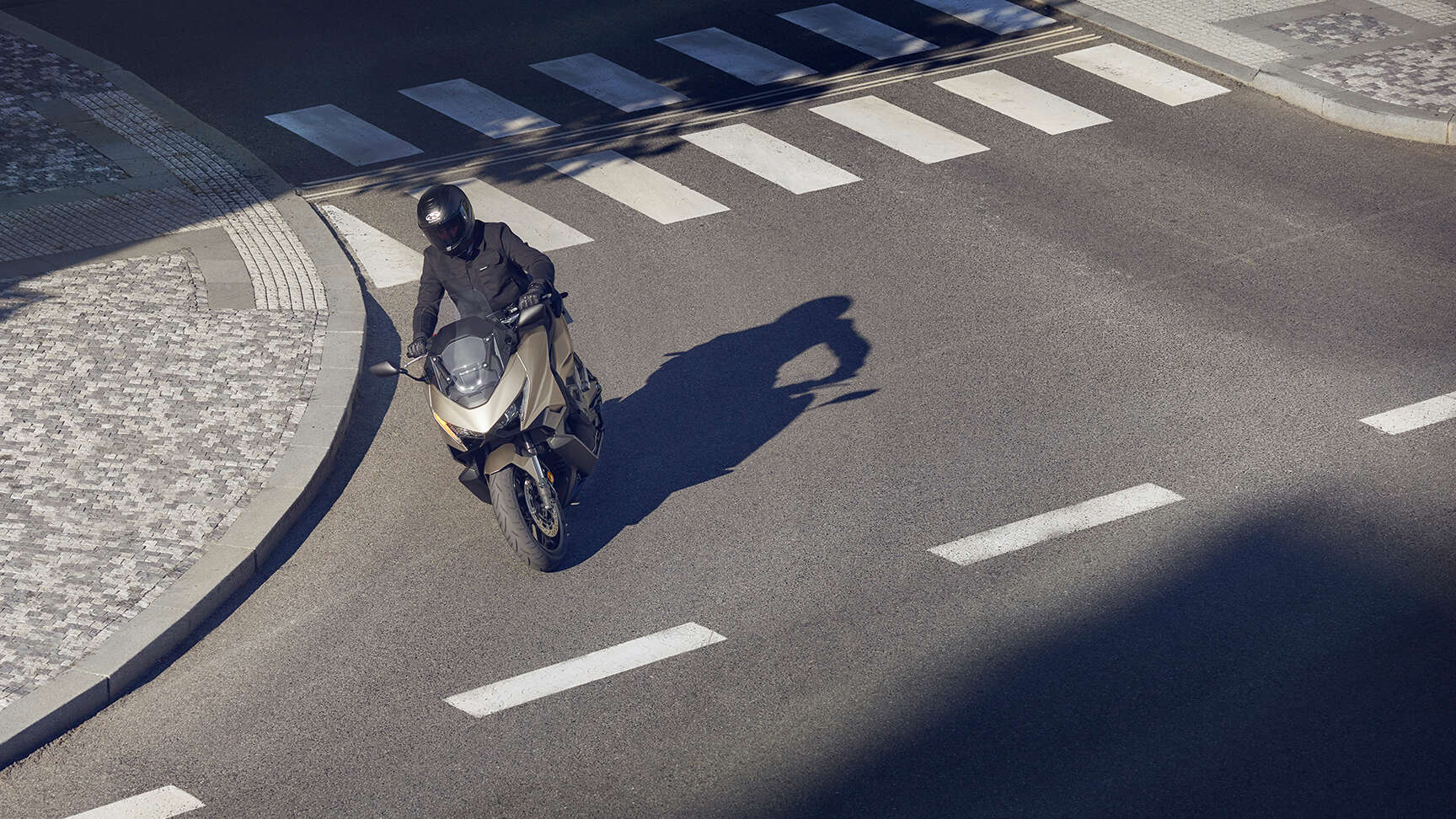 fb_r (2) Ein Motorradfahrer auf einem goldenen Motorrad FORZA 750 fährt über einen Zebrastreifen.