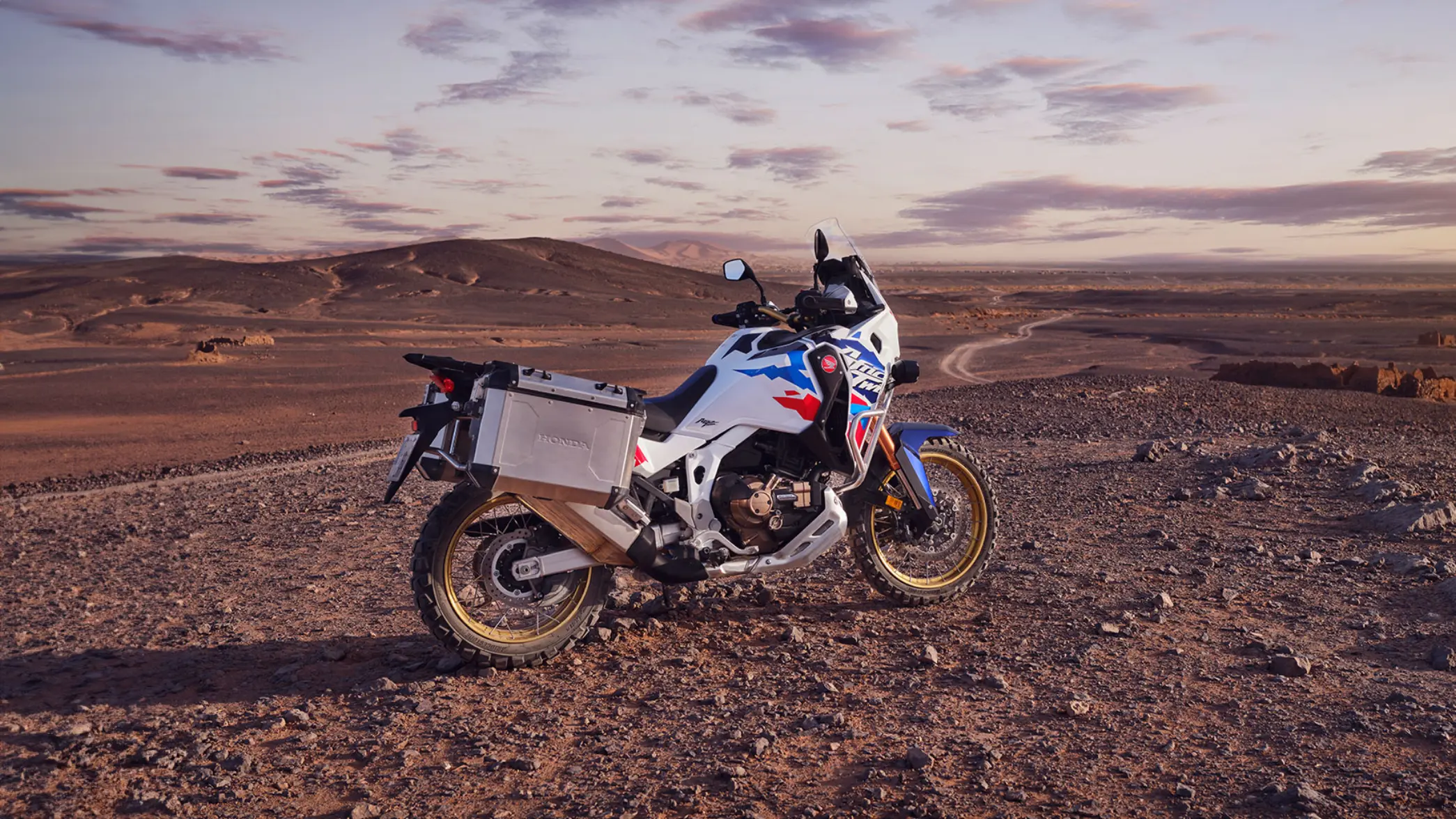 Ein Honda Motorrad AFRICA TWIN ADVENTURE steht in einer weiten, steinigen Wüstenlandschaft.