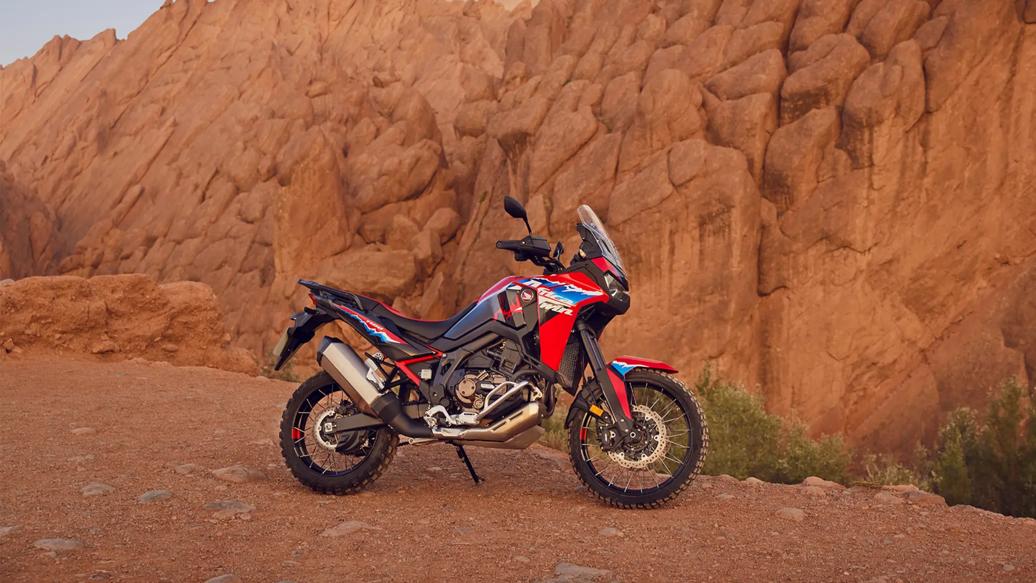 fb_r_w (1) Eine rote Honda Africa Twin steht vor einer felsigen Landschaft.