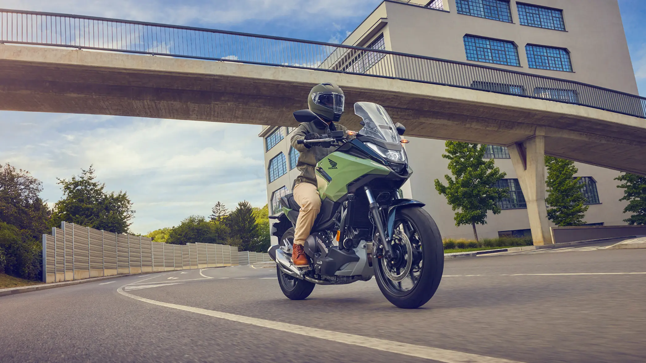 fb_r_w (1) Ein Motorradfahrer fährt eine grüne Honda NC750X auf einer Straße unter einer Brücke.
