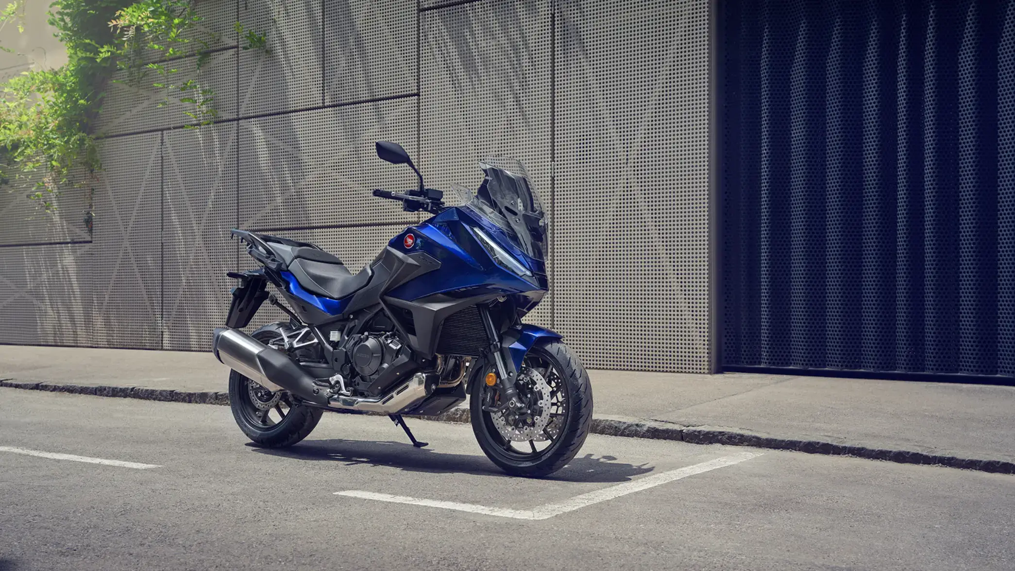 Eine blaue Honda NT1100 steht auf einem Parkplatz vor einer modernen Wand.