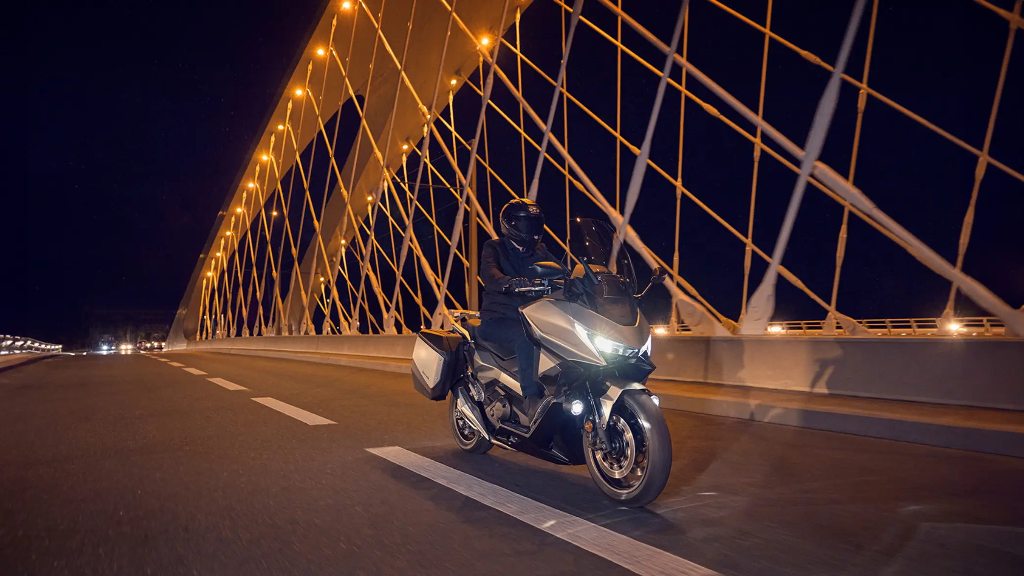 Ein Motorradfahrer fährt bei Nacht über eine beleuchtete Brücke.