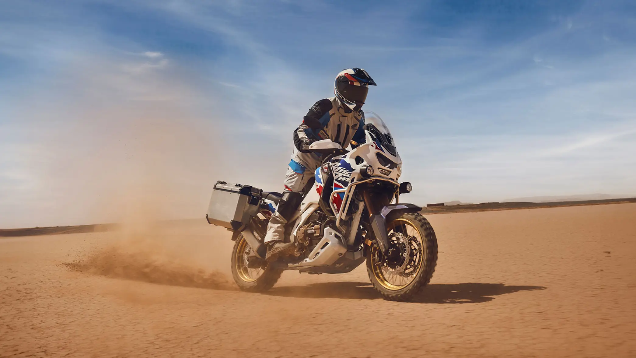 Ein Motorradfahrer fährt eine Honda Africa Twin durch eine staubige Wüstenlandschaft.