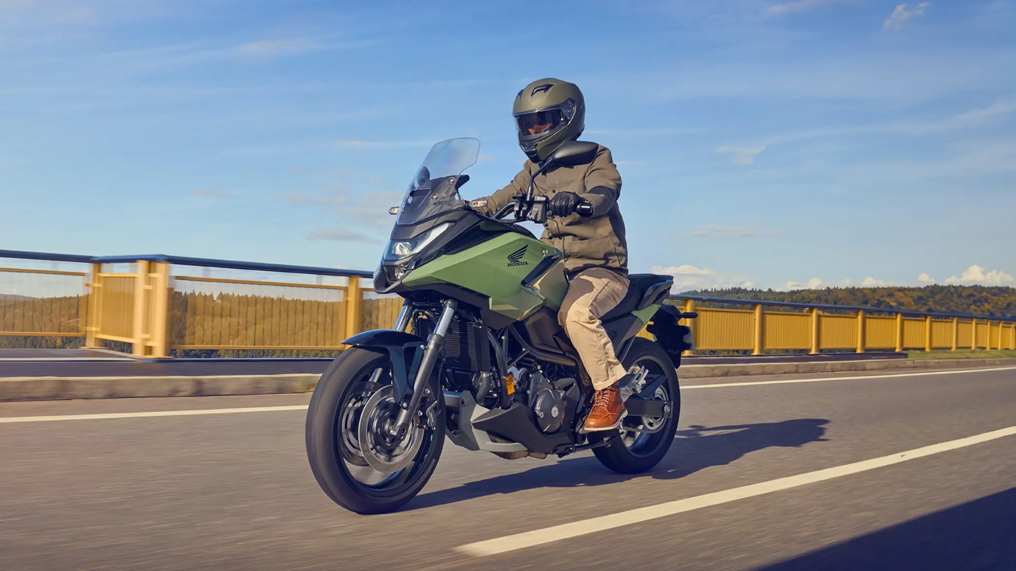 Eine Person fährt ein grünes Honda-Motorrad NC750X auf einer Straße.