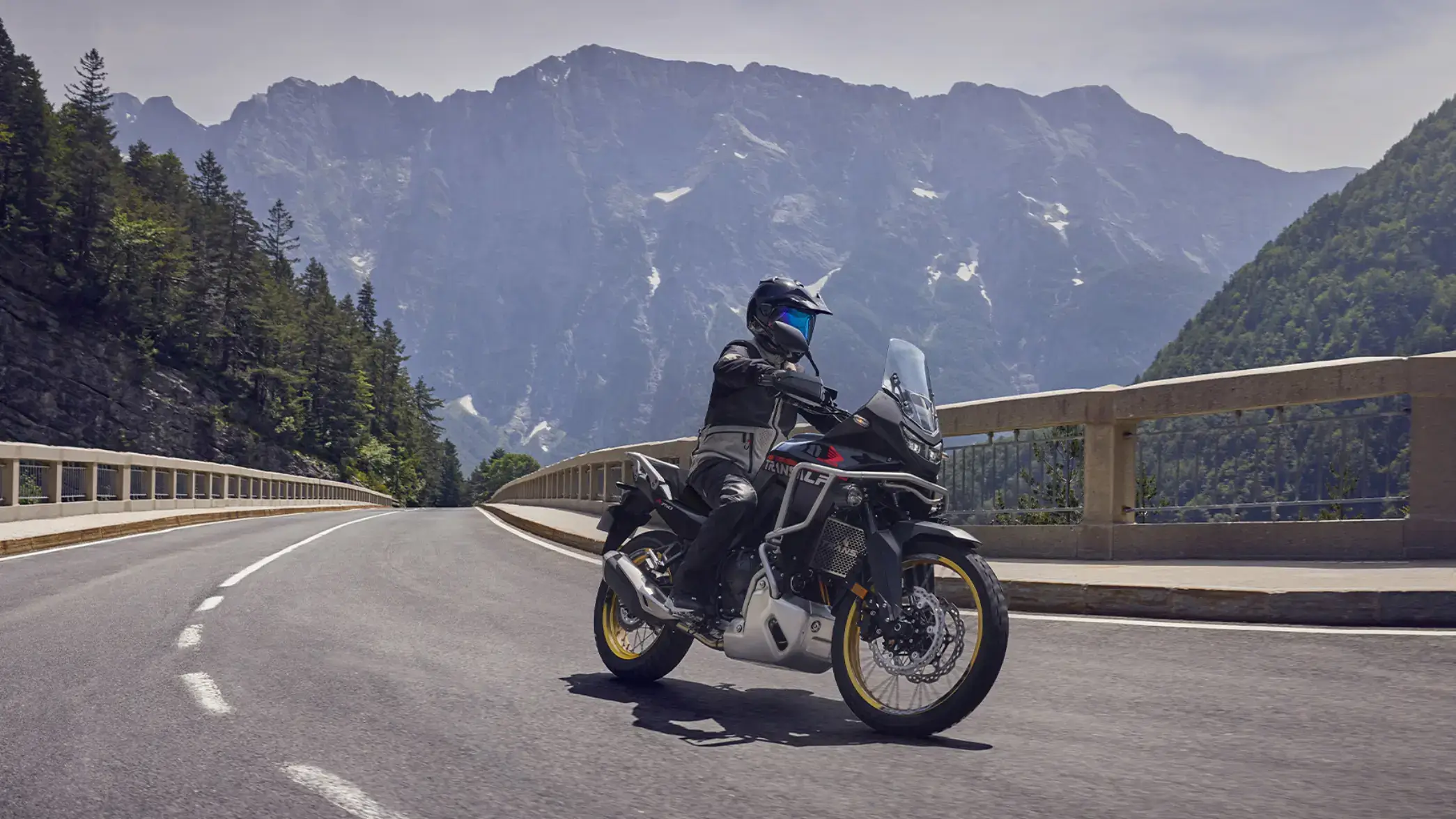 Ein Motorradfahrer fährt eine Honda Transalp auf einer kurvigen Bergstraße.