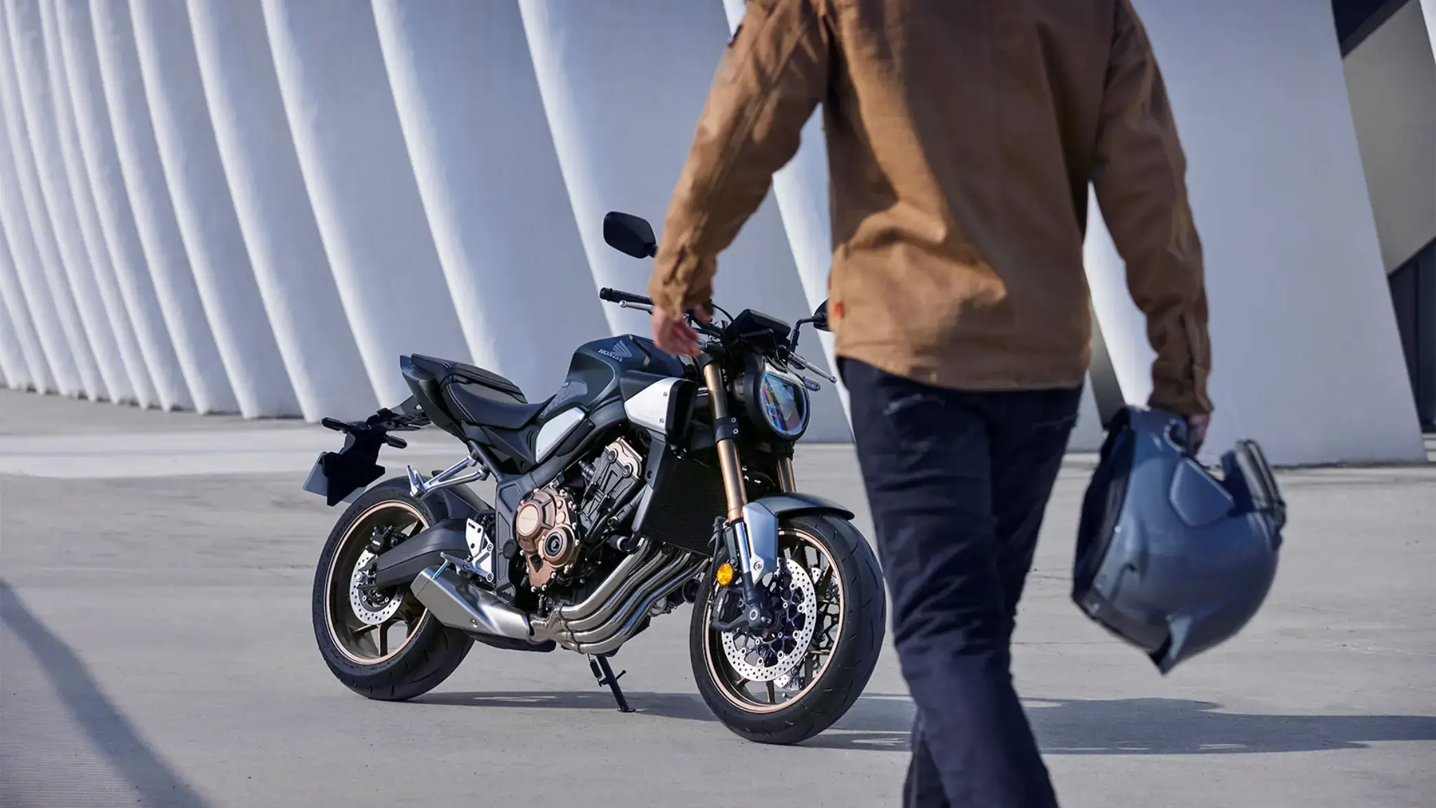 Eine Person geht auf ein geparktes CB650R zu und hält einen Helm in der Hand.