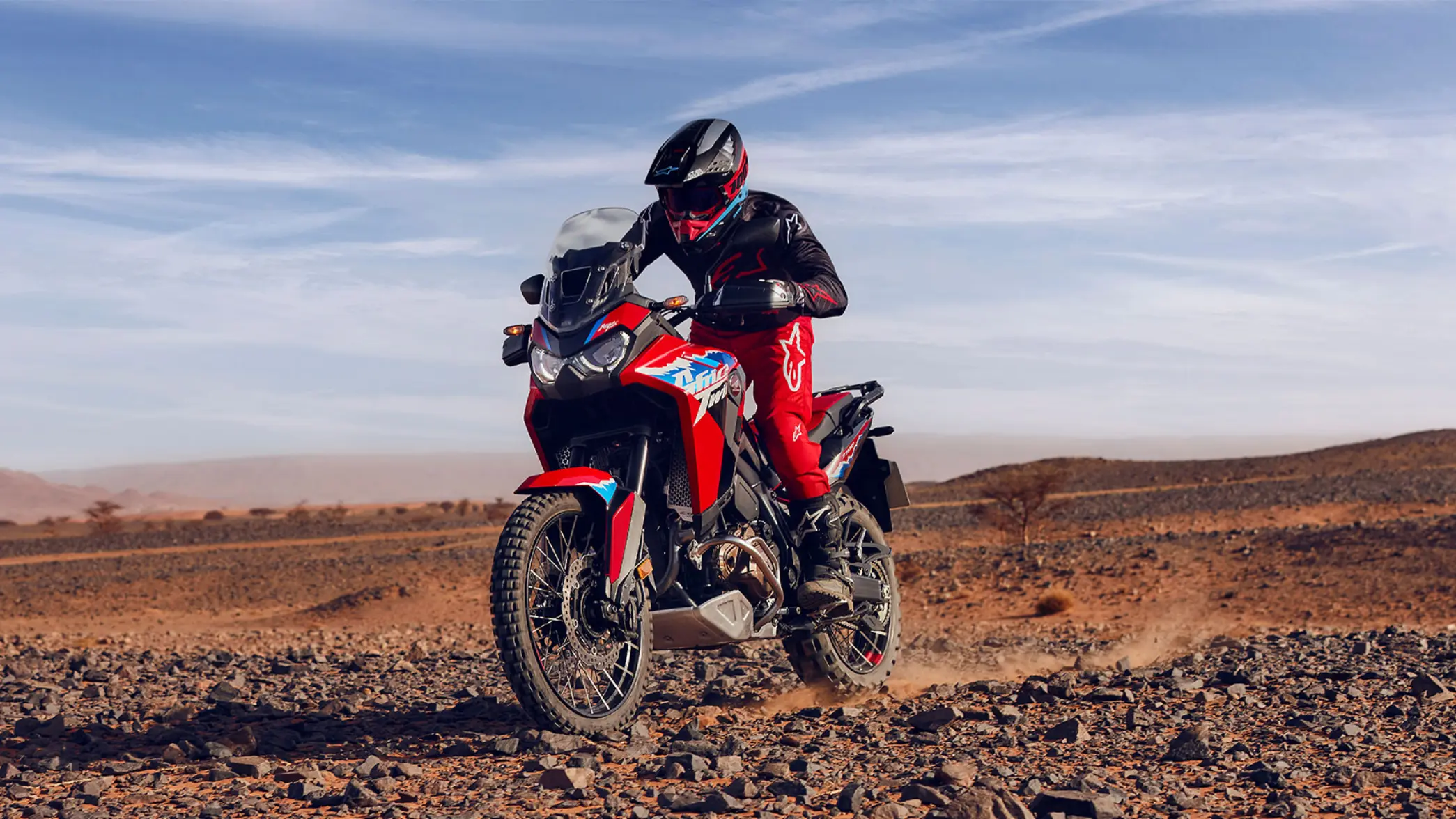 Eine Person fährt eine Honda Africa Twin durch eine steinige Wüstenlandschaft.