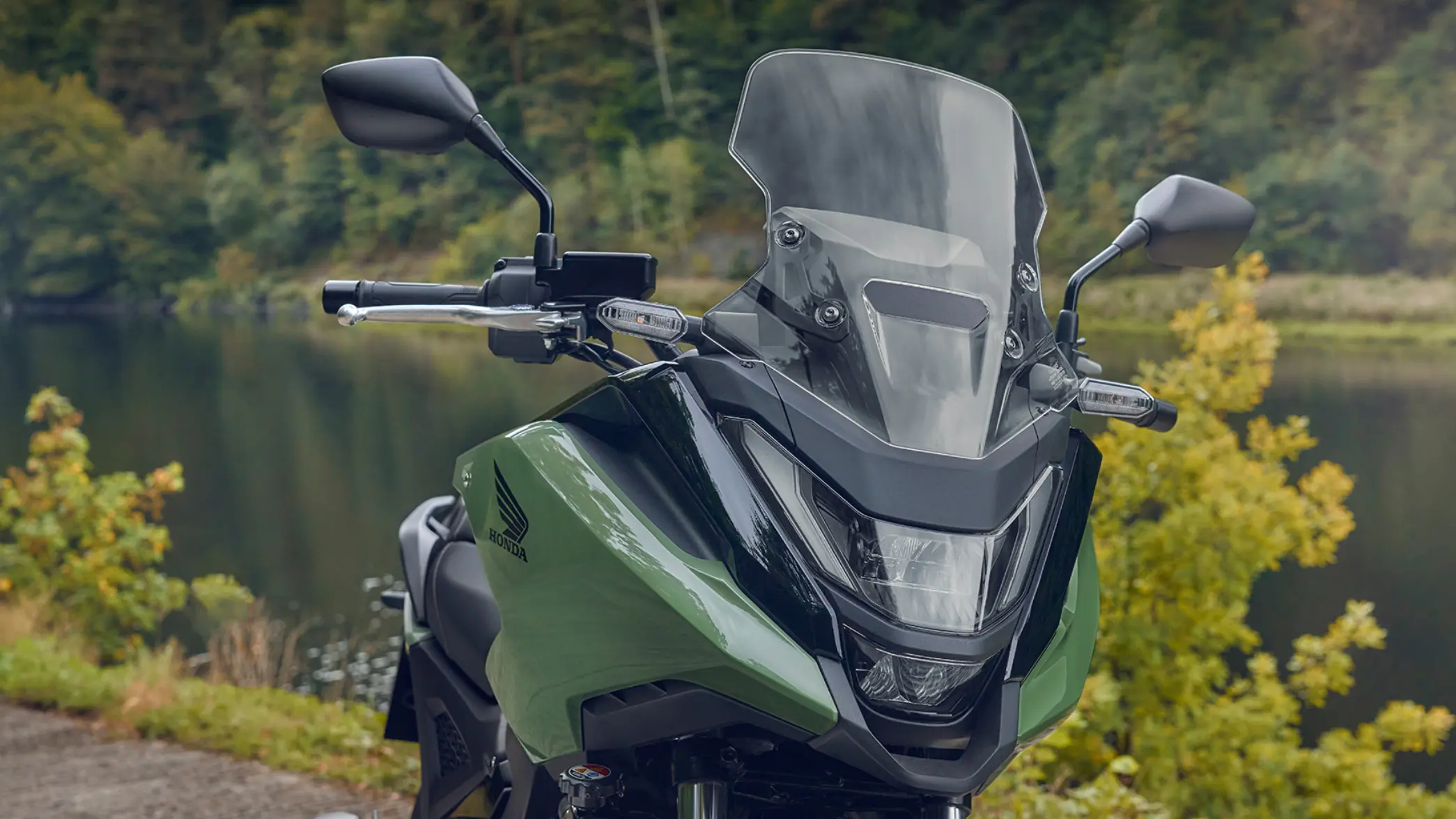 fb_r_w Ein grünes Honda-Motorrad NC750X steht vor einem bewaldeten Hintergrund.