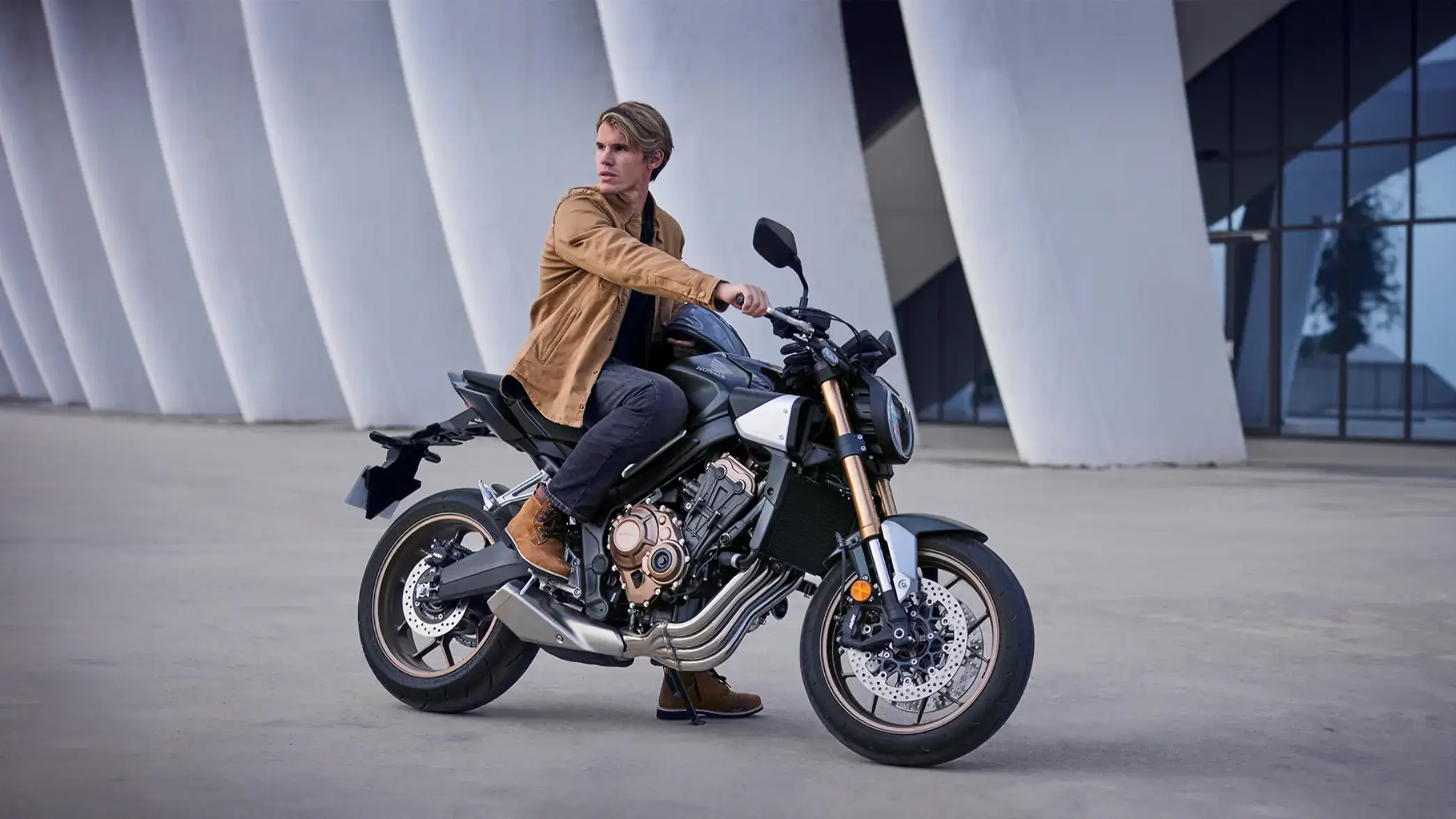 Ein Mann sitzt auf einem Honda-Motorrad CB650R vor einer modernen Architektur.