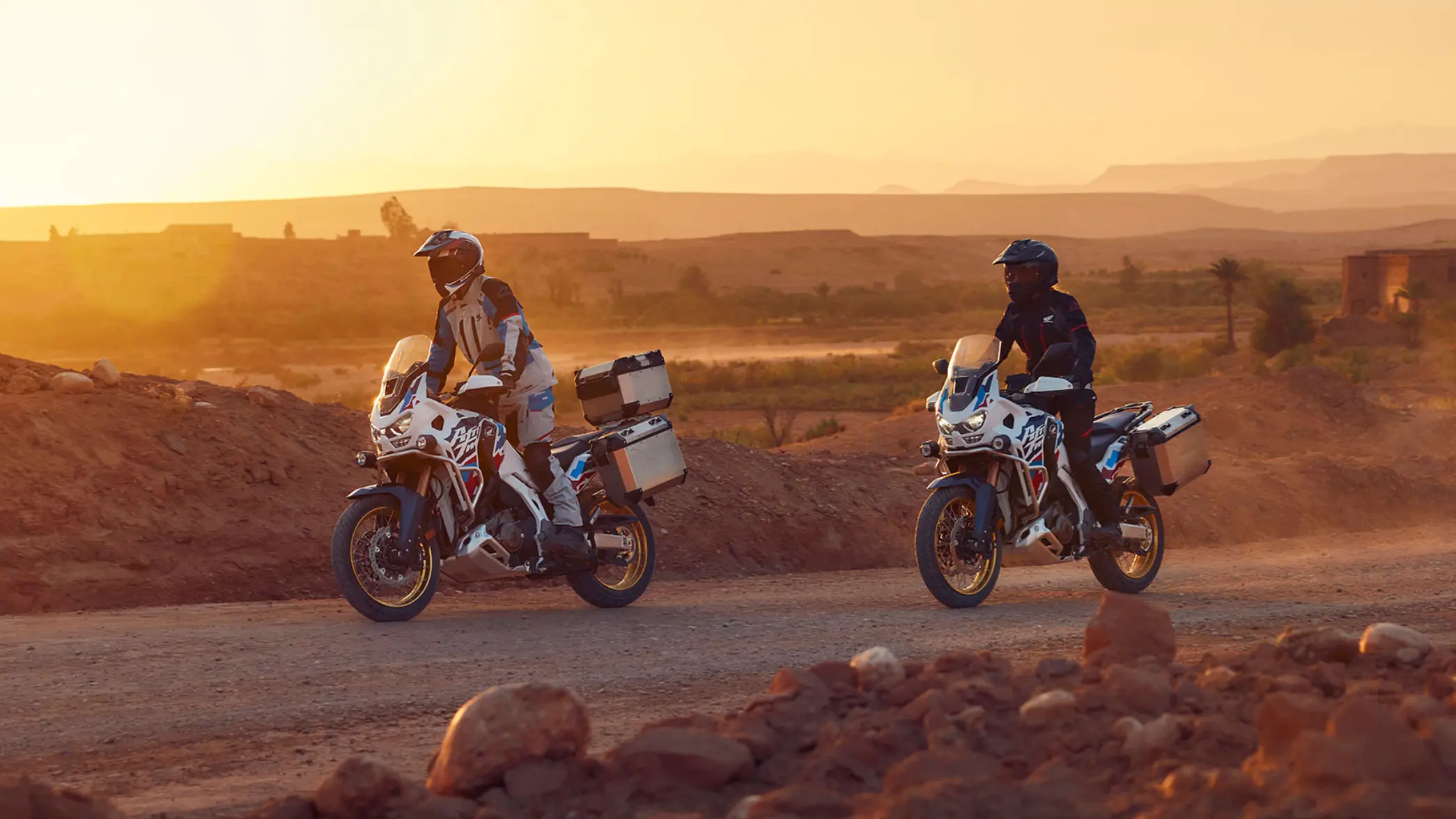 fb_r_w (4) Zwei Personen fahren auf Honda Africa Twin Motorrädern bei Sonnenuntergang durch eine Wüstenlandschaft.
