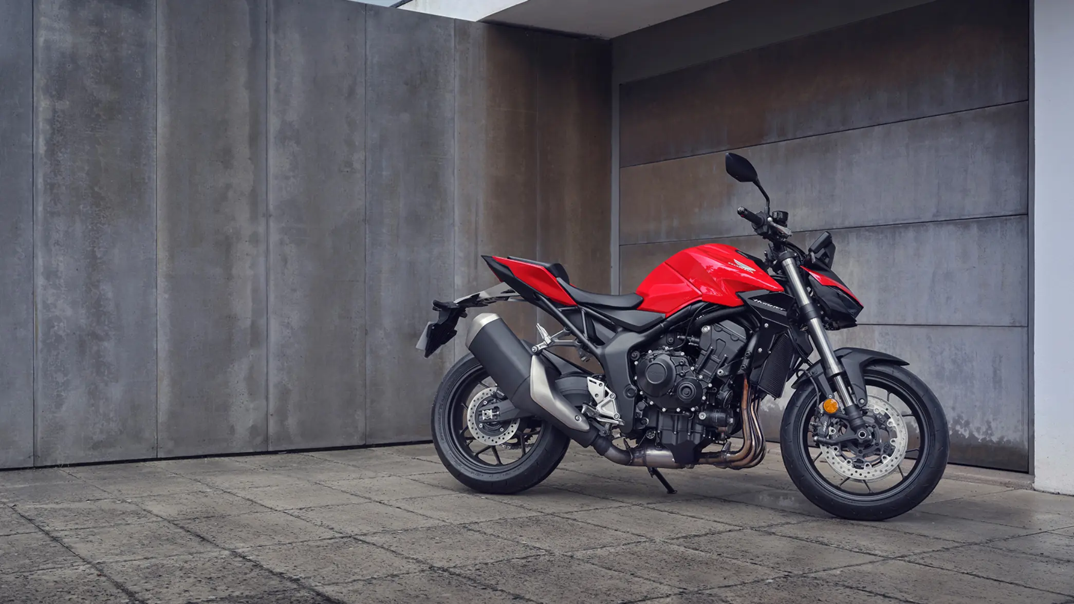 Ein rotes Motorrad CB1000 Hornet steht vor einer grauen Betonwand.