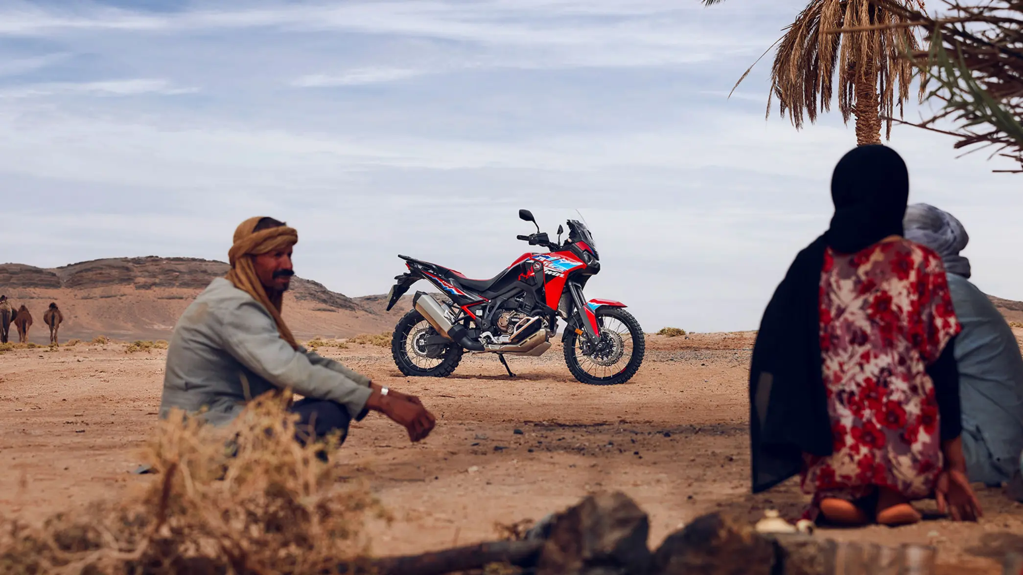 Motorrad Honda Africa Twin in einer Wüstenlandschaft mit sitzenden Menschen im Vordergrund.