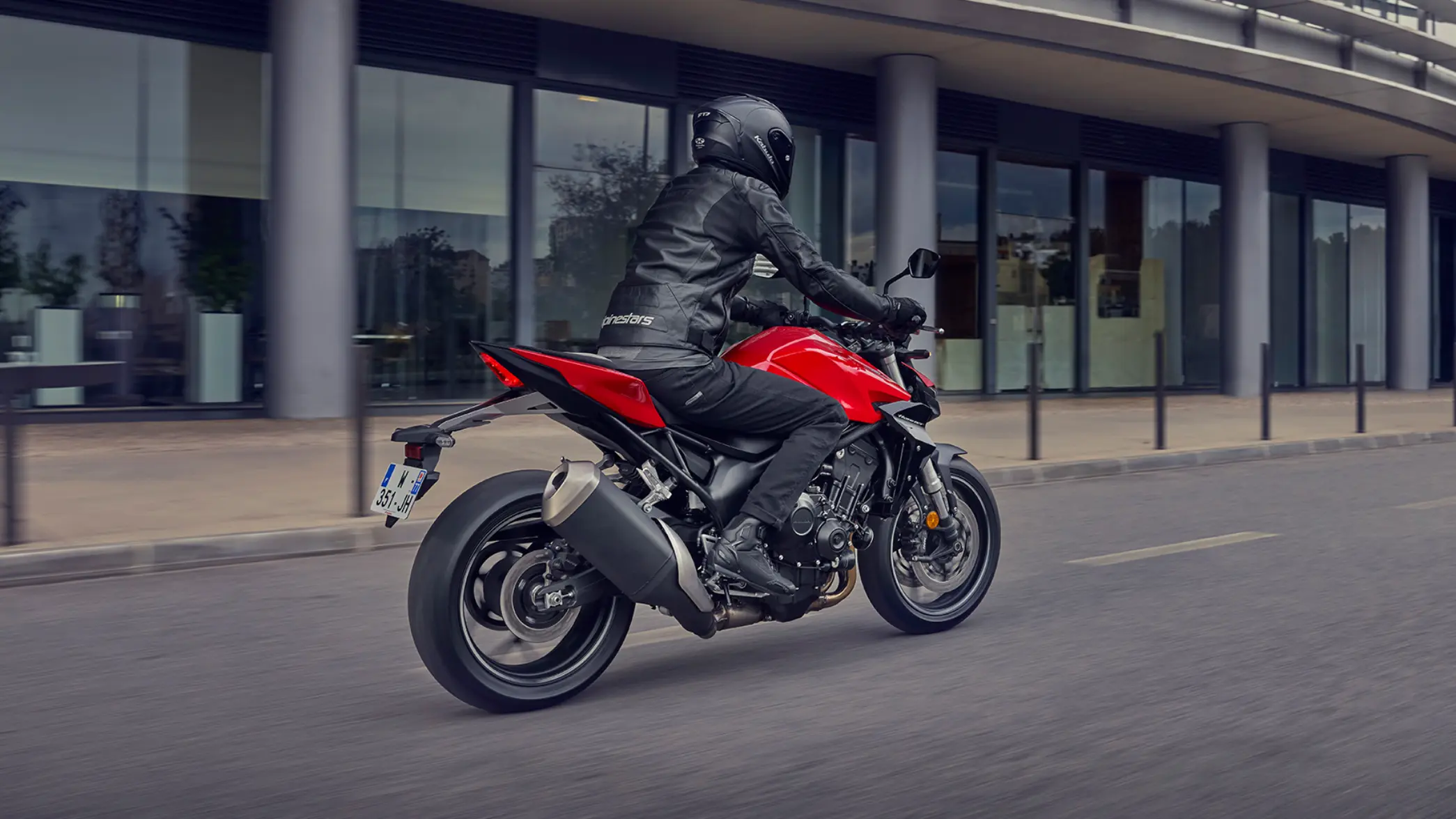 Ein Motorradfahrer fährt auf einer roten Honda CB750 Hornet auf einer Straße.