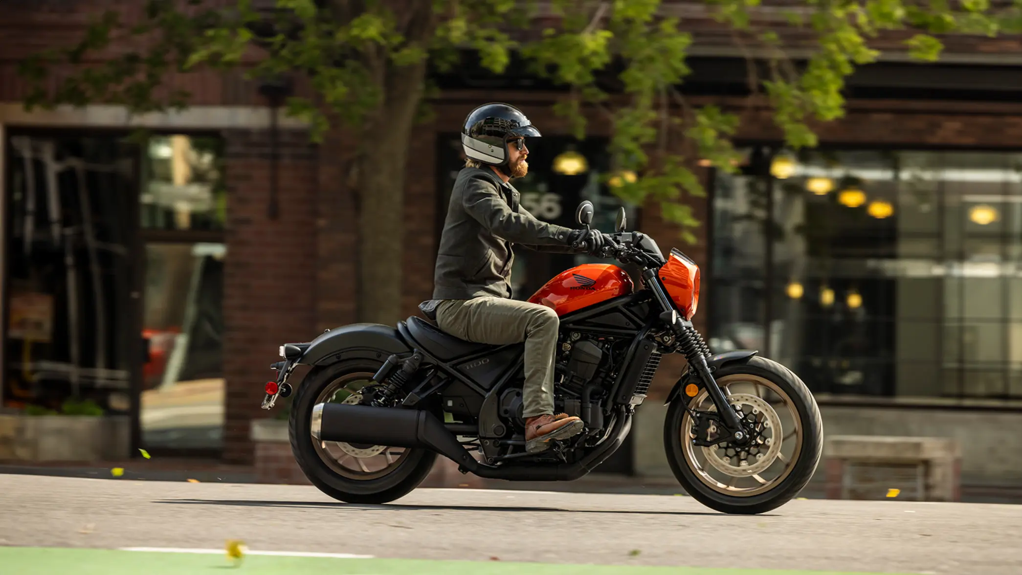 Ein Mann fährt eine orangefarbene Honda Rebel 1100 auf der Straße.