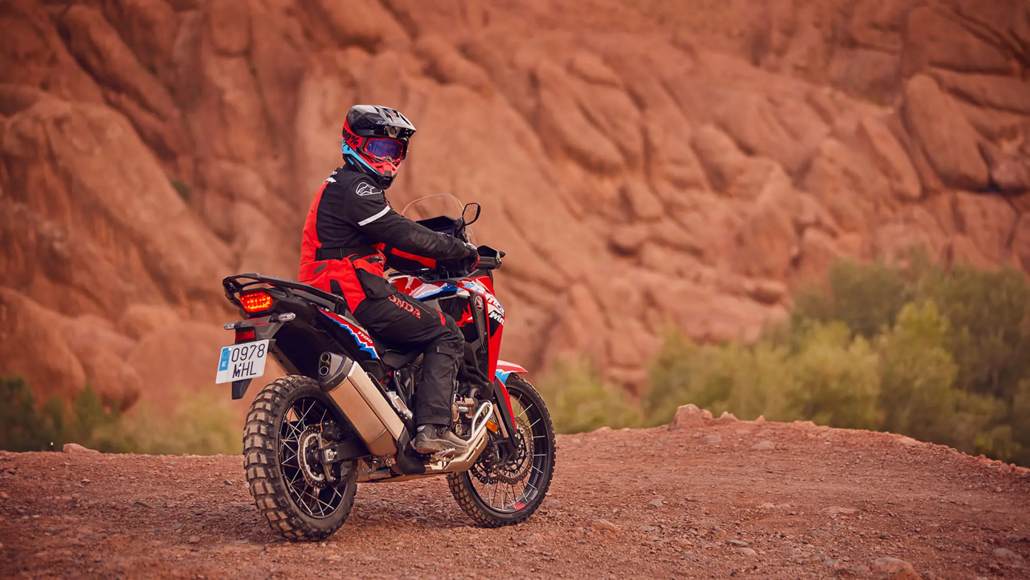 Ein Motorradfahrer auf einer Honda Africa Twin fährt durch eine felsige Wüstenlandschaft.