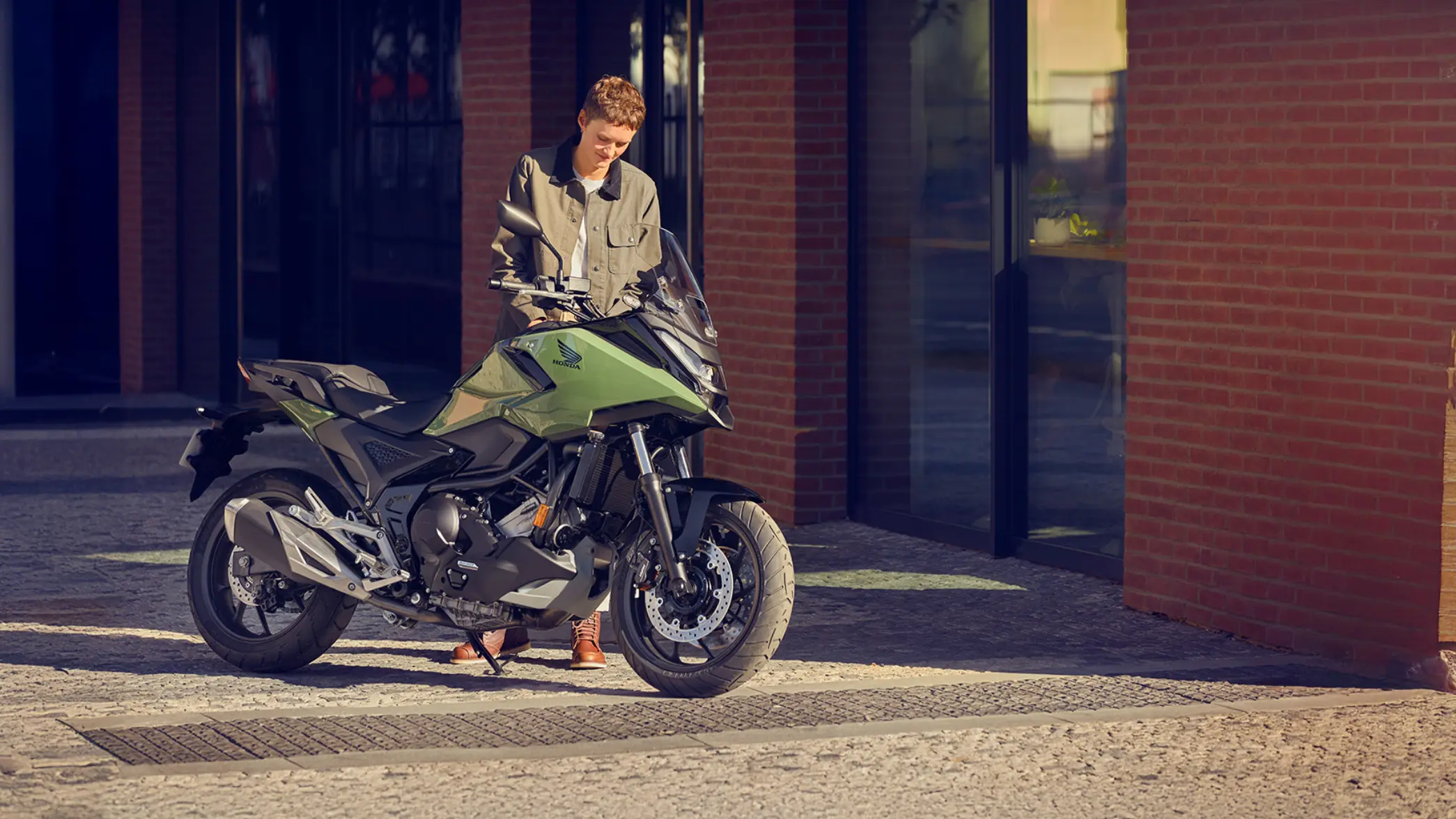 Eine Person steht neben einem grünen Honda-Motorrad NC750X vor einem Gebäude.