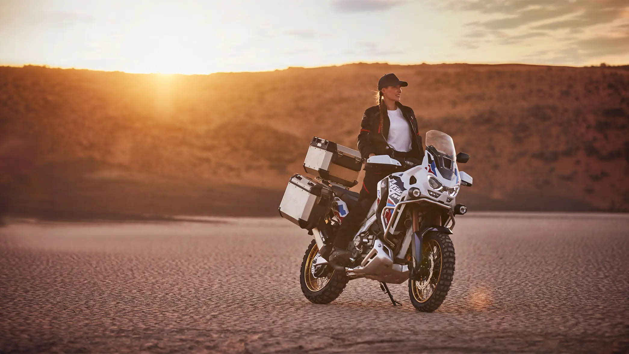 fb_r_w (7) Eine Person sitzt auf einem Honda Africa Twin Motorrad in einer Wüstenlandschaft bei Sonnenuntergang.