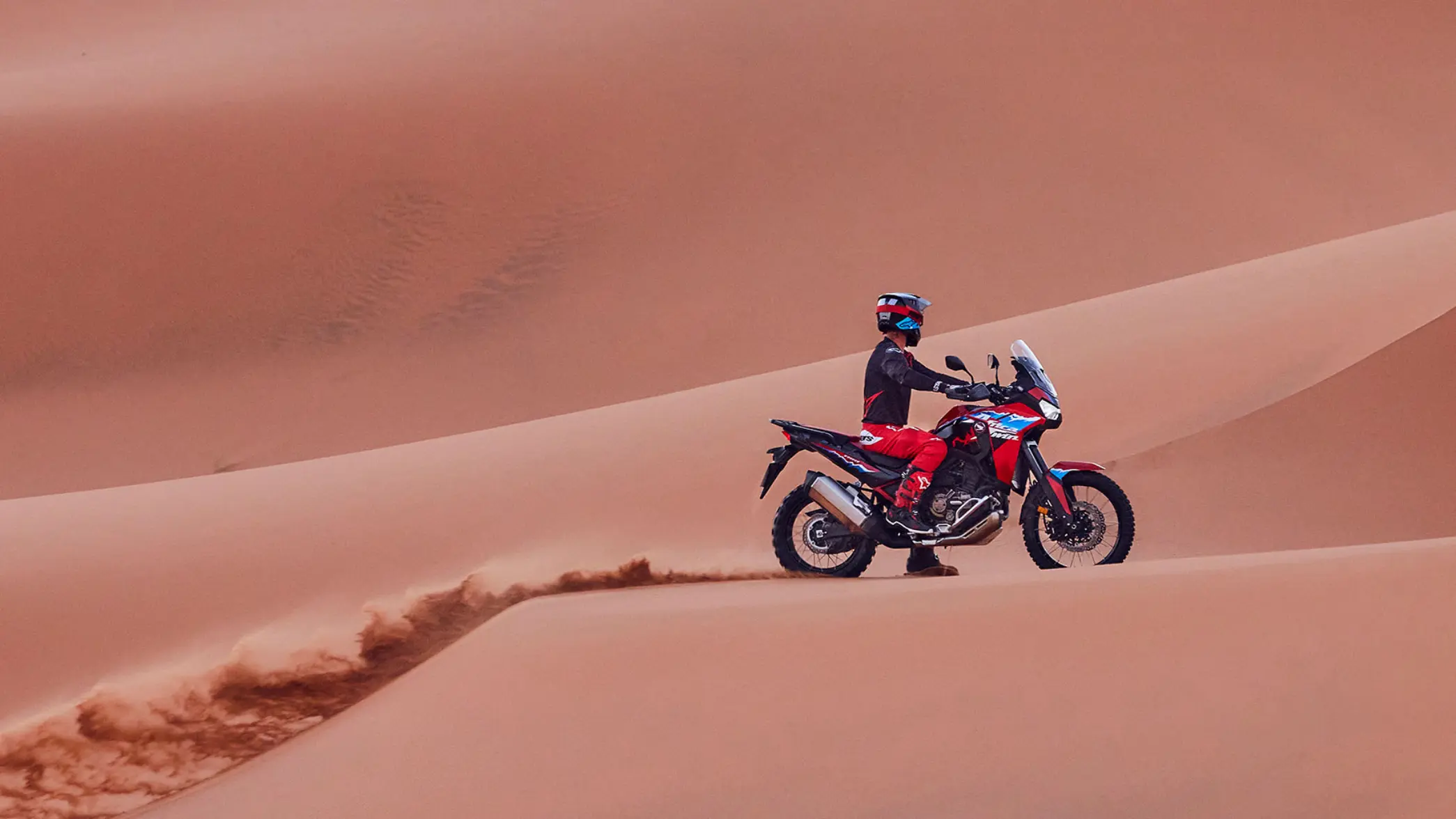 Ein Motorradfahrer fährt mit einer Honda Africa Twin durch eine Sanddüne.