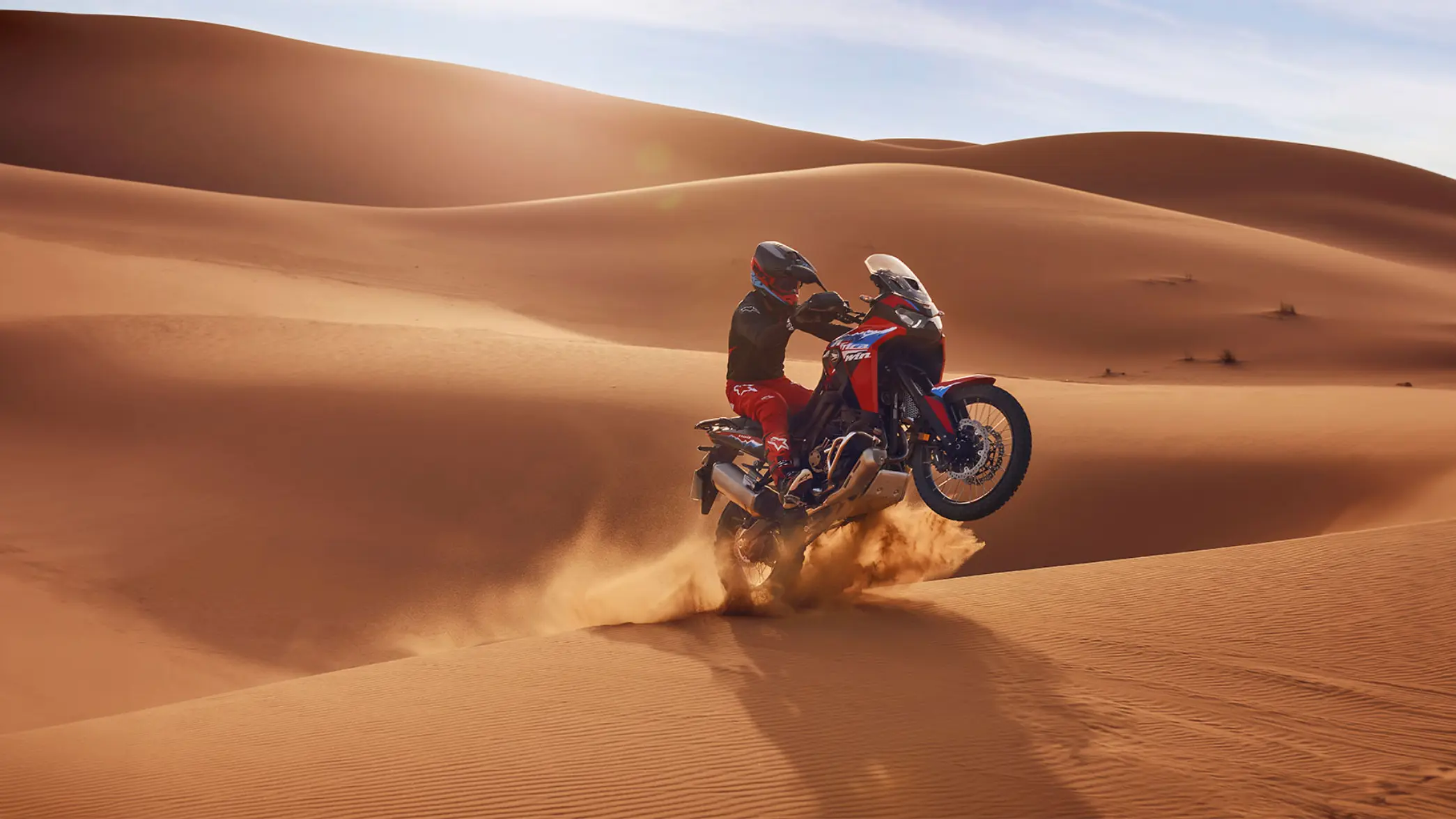 Ein Motorradfahrer fährt mit einer Honda Africa Twin durch eine Sanddüne in der Wüste.