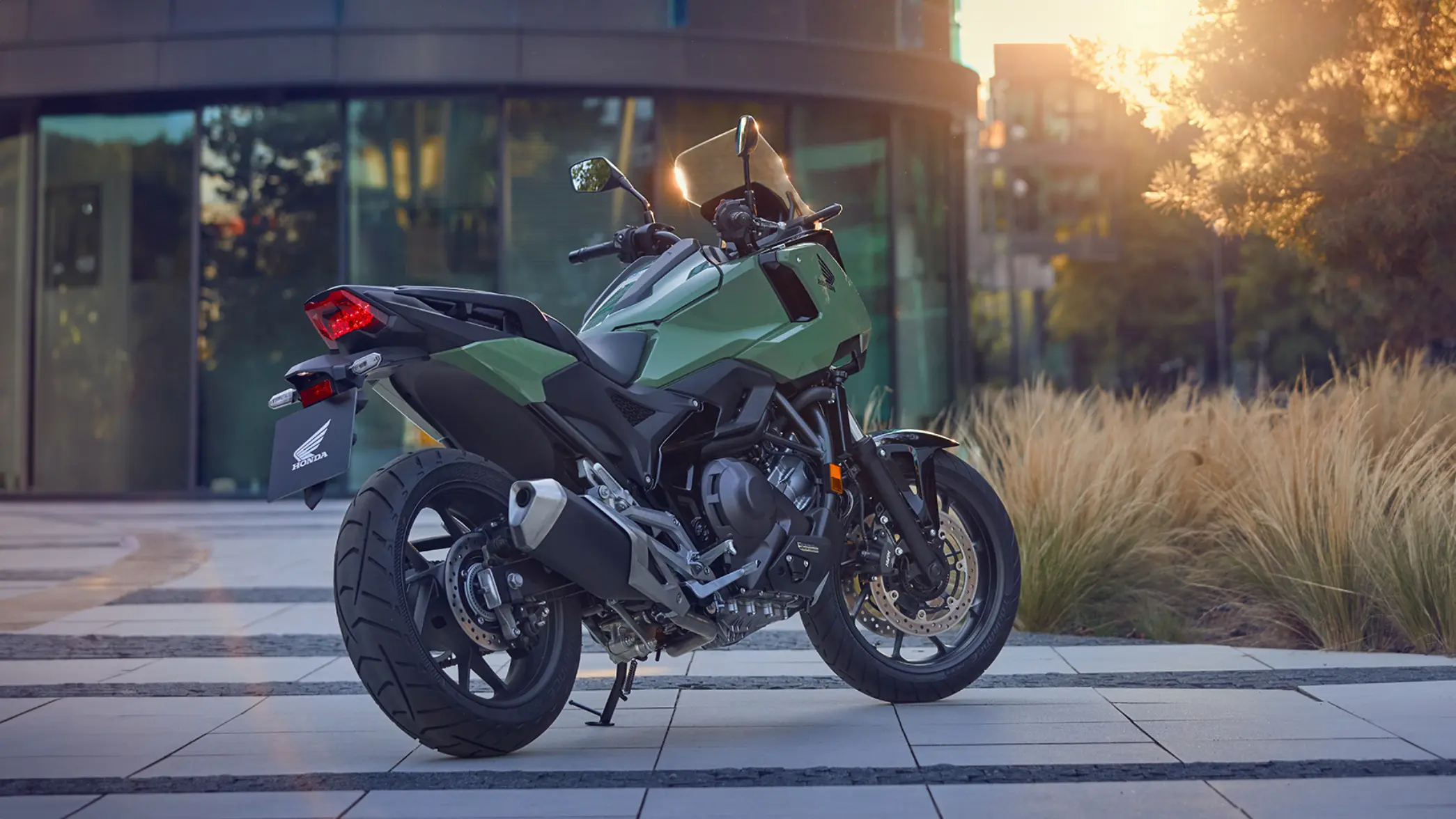 fb_r_w (9) Ein grünes Honda-Motorrad NC750X steht auf einem gepflasterten Platz bei Sonnenuntergang.