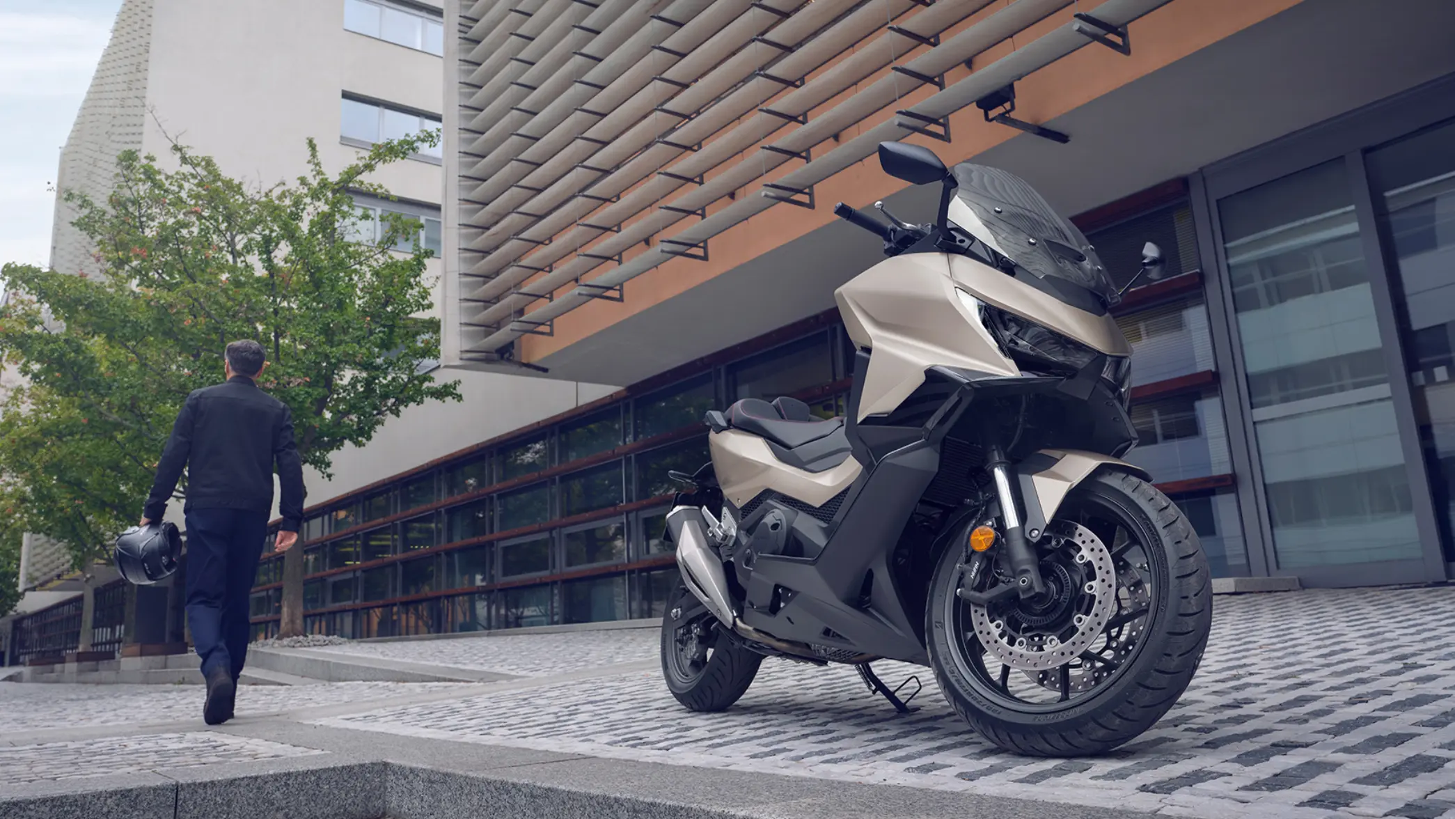 Eine Honda FORZA 750 steht vor einem Gebäude, während ein Mann mit Helm weggeht.
