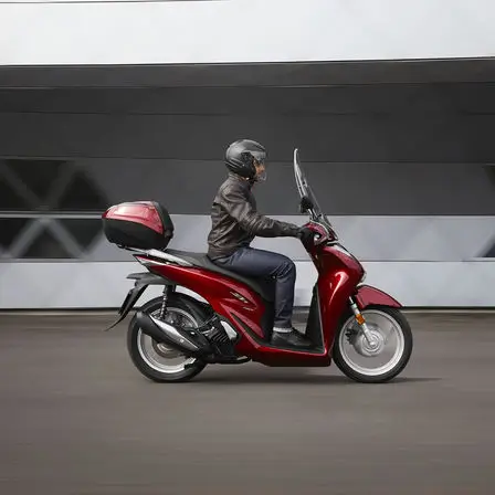 Ein Motorradfahrer fährt eine rote Honda SH150i.