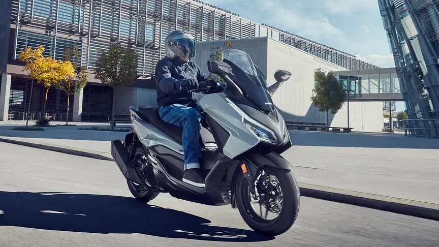 Ein Fahrer auf einem Honda Forza 125 Roller fährt durch eine städtische Umgebung.