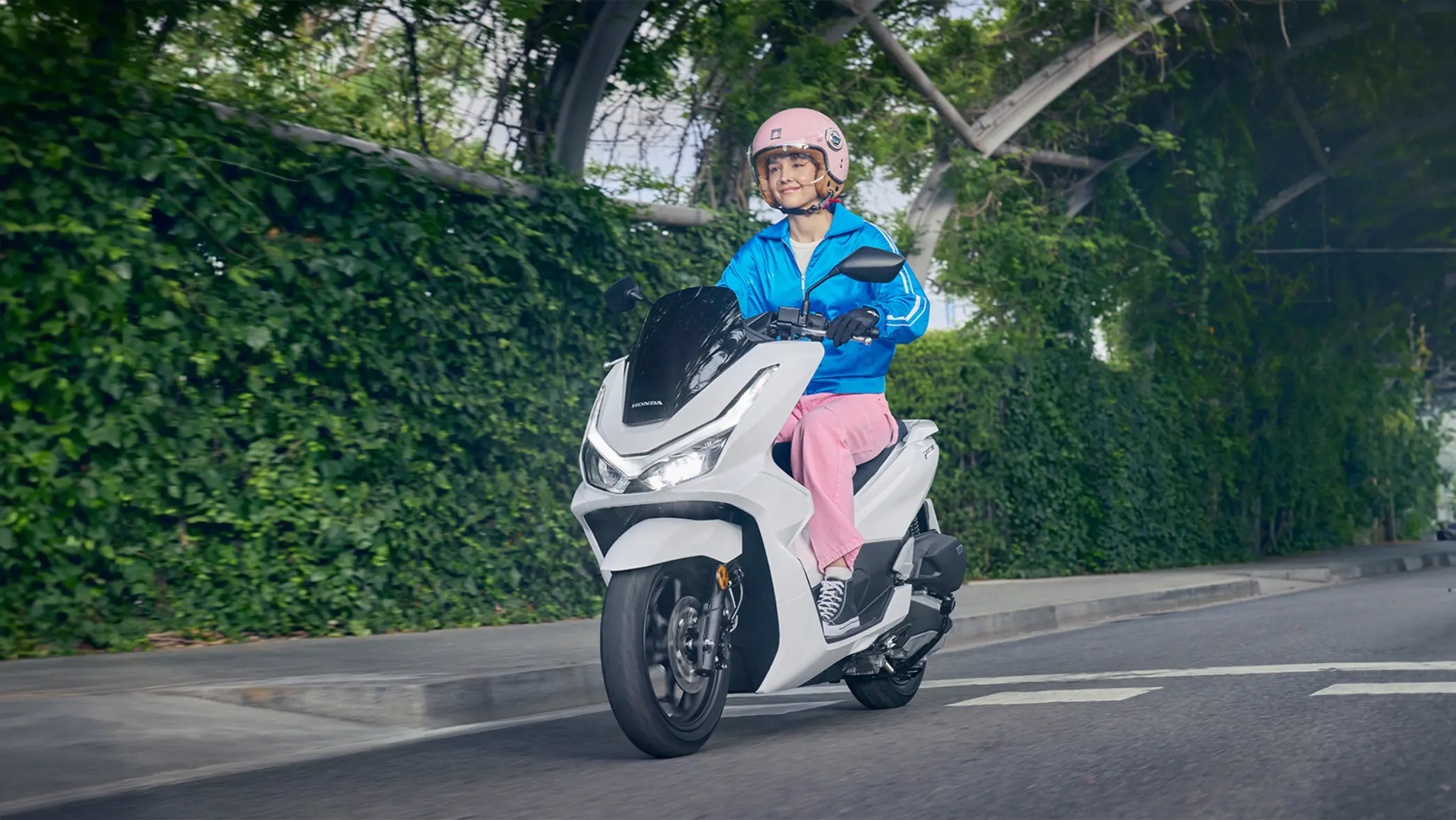 Eine Person fährt einen weißen Honda PCX125 Roller auf einer Straße entlang.