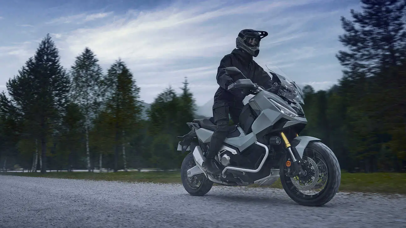 Ein Fahrer auf einem Honda X-ADV Motorrad fährt auf einer Schotterstraße durch eine bewaldete Landschaft.